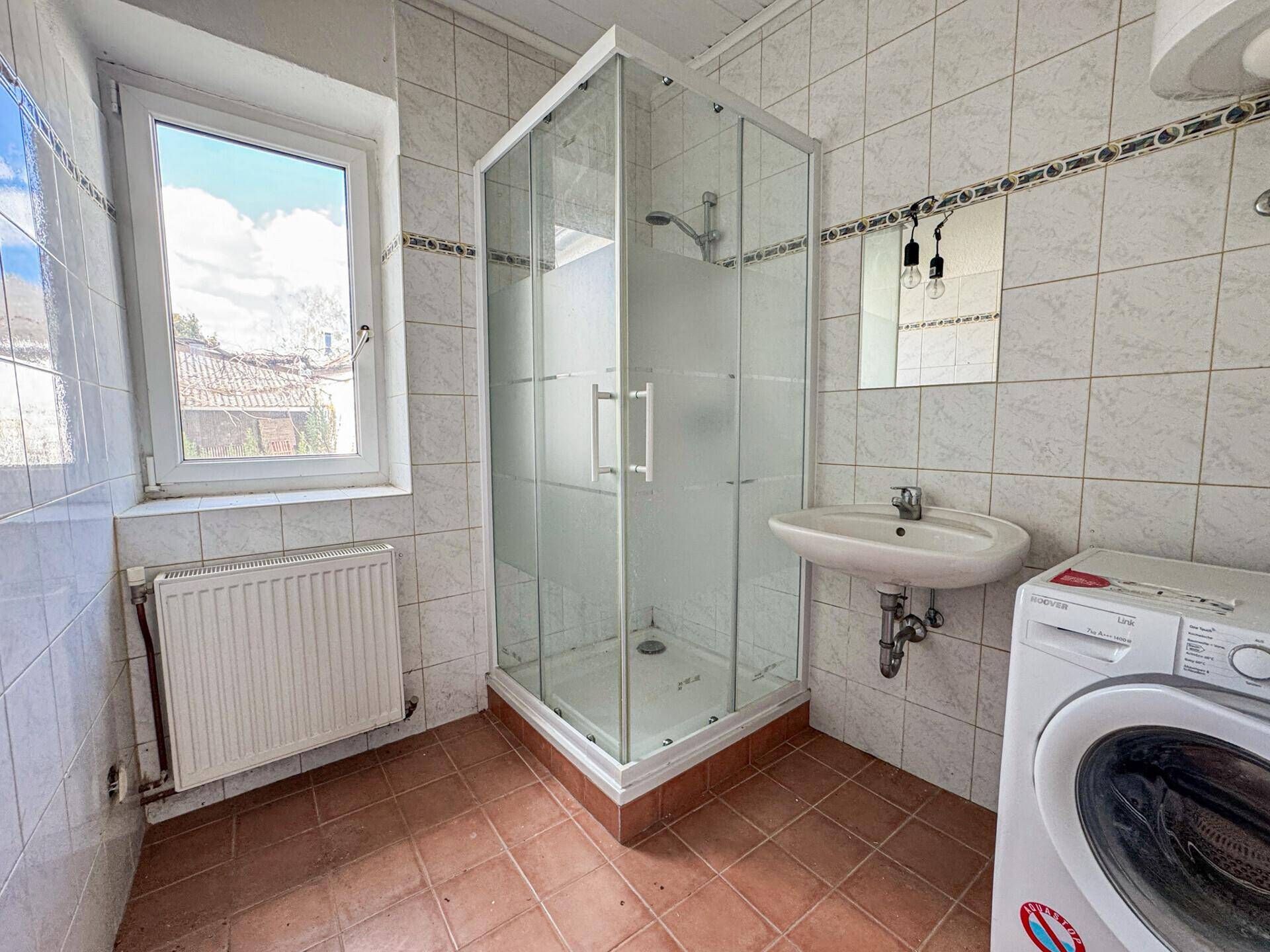Badezimmer mit Duschkabine, Waschbecken und Waschmaschine, hell gefliest.