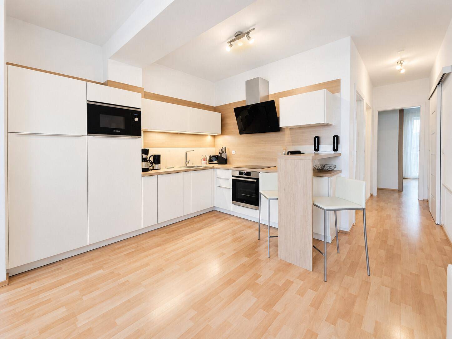 Moderne Einbauküche in Weiß und Holzoptik mit integrierten Geräten und Frühstücksbar.