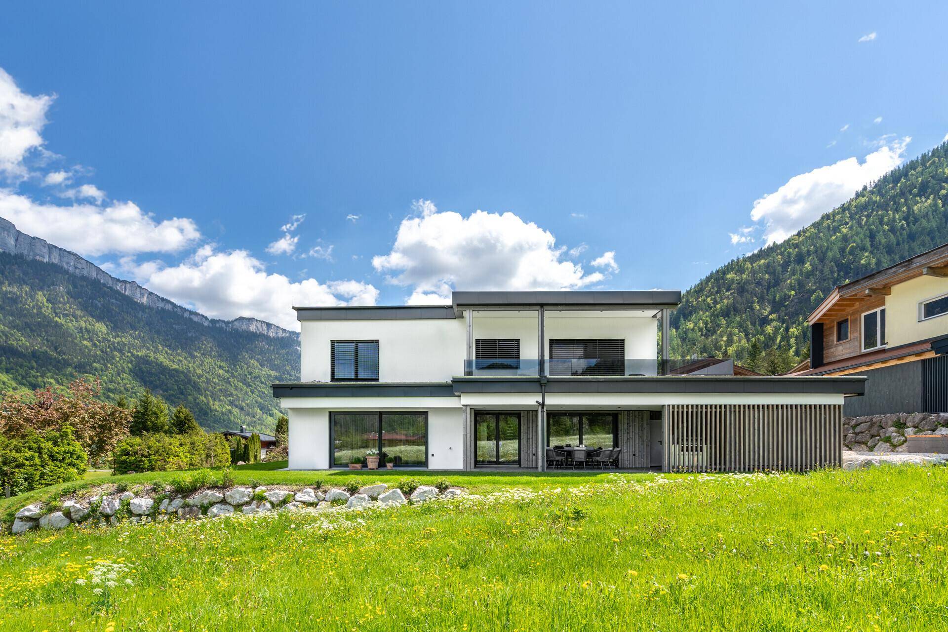 Rückansicht der modernen Villa mit großer Terrasse, Garten und beeindruckendem Bergblick.