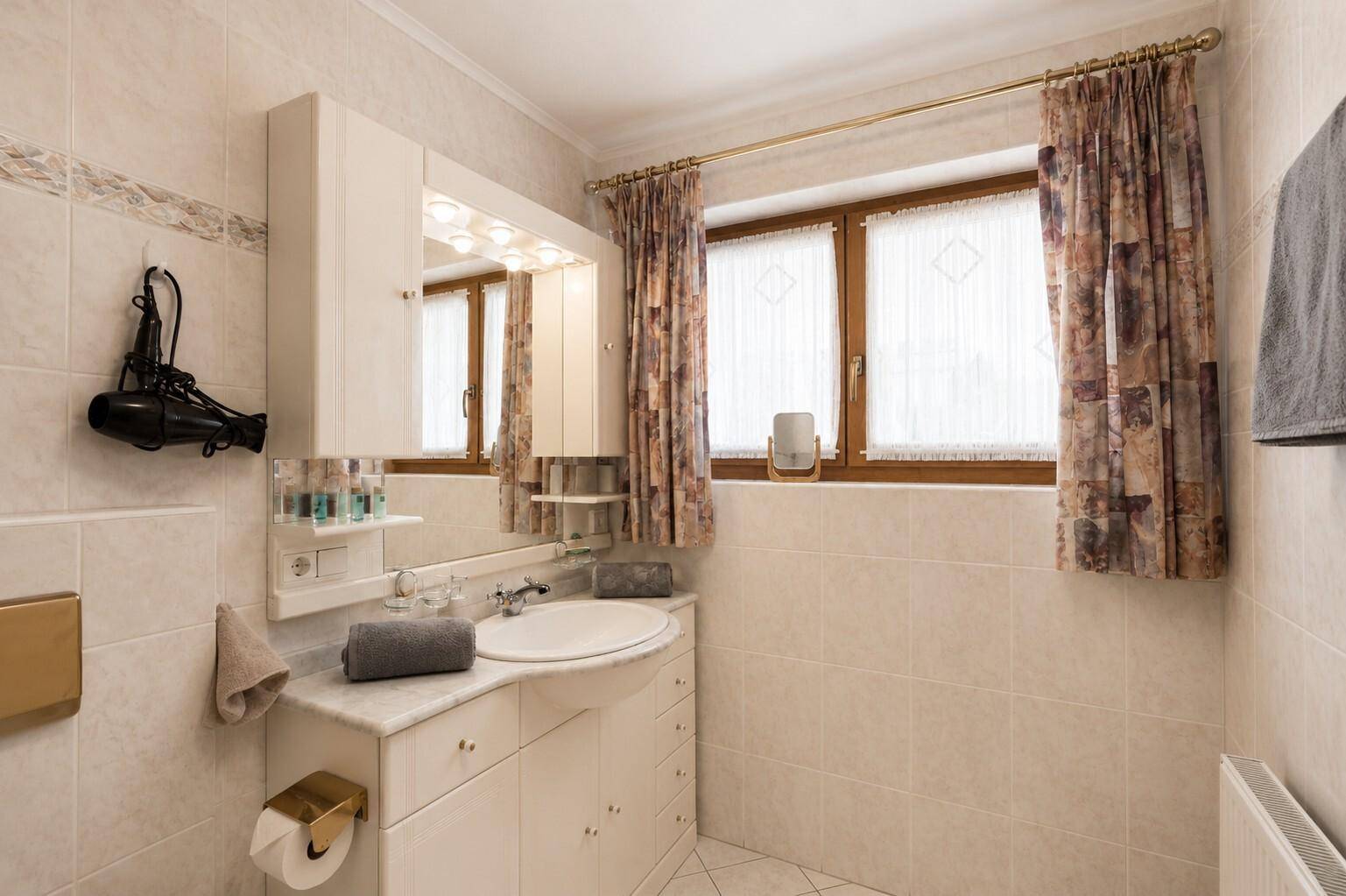 Helles Badezimmer mit Waschtisch, Spiegelschrank und Fenster für natürliches Licht.