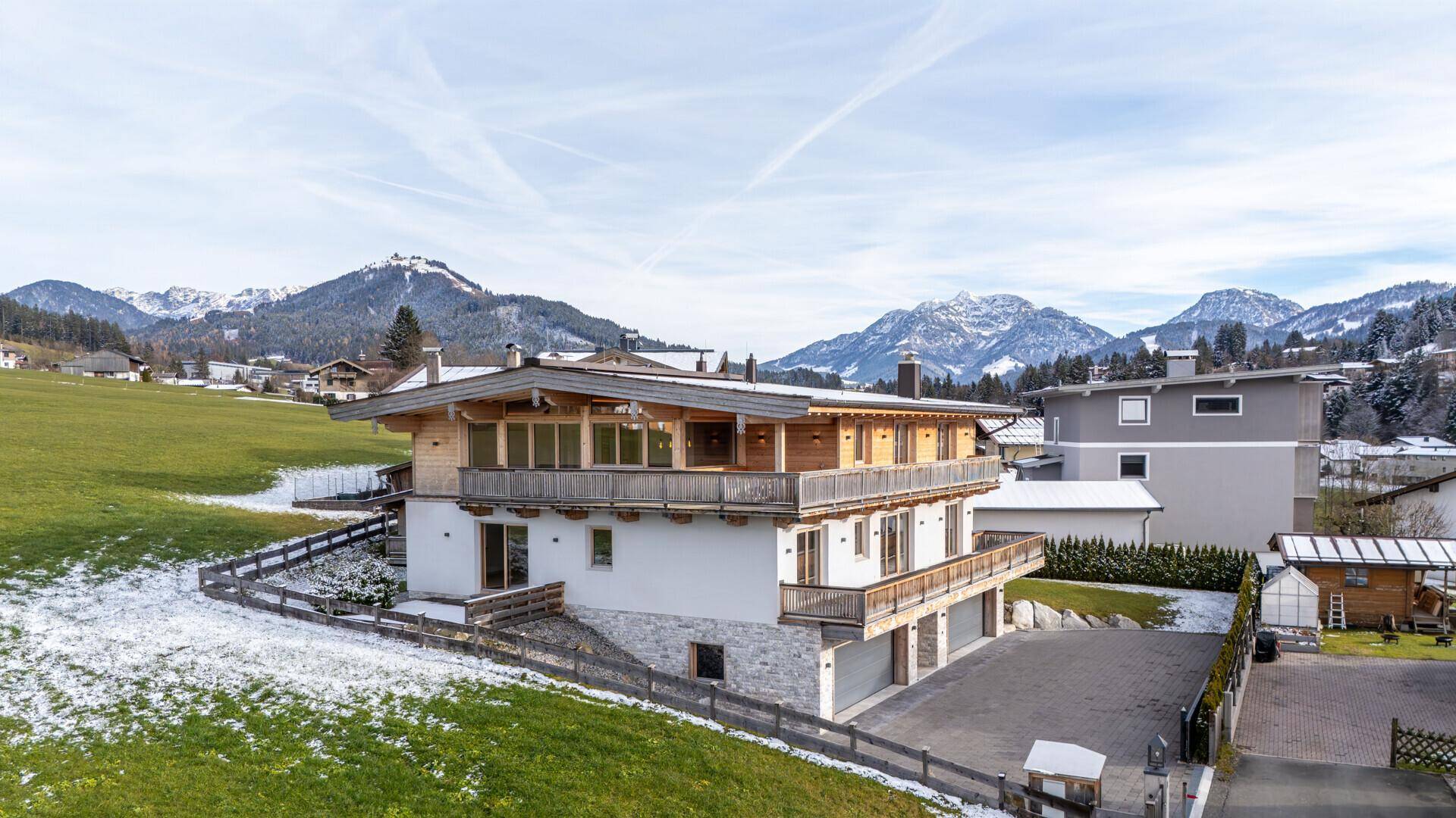 Ansicht des modernen Chalets mit Holzbalkonen und schneebedeckten Bergen in der Ferne.