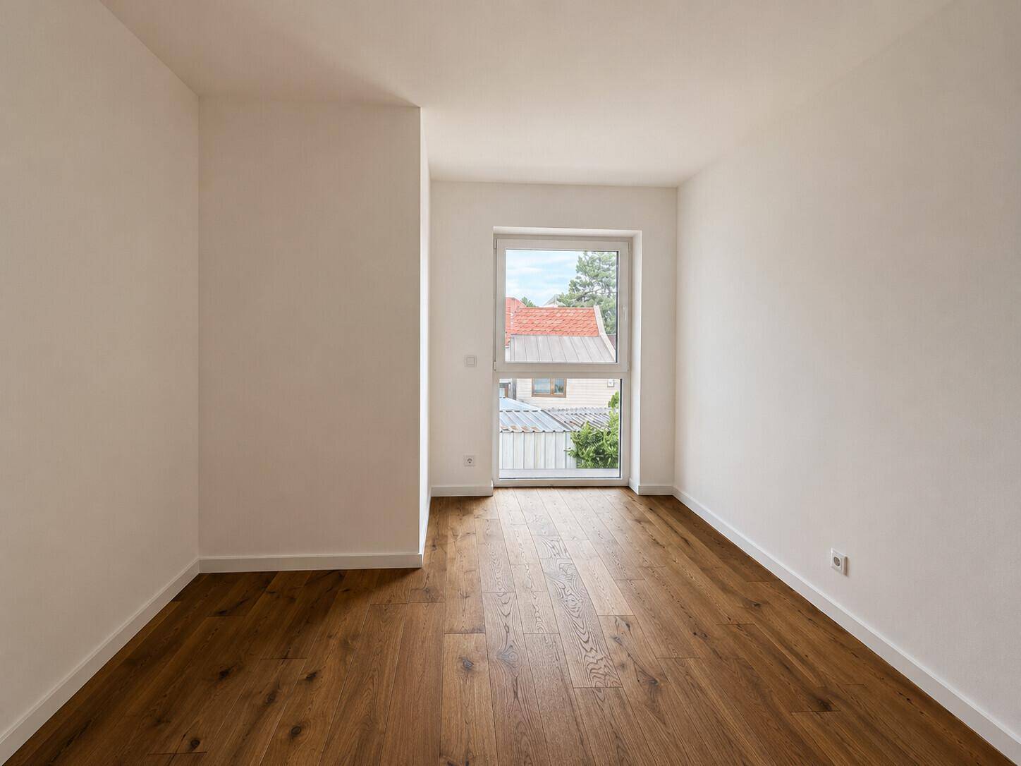 Unmöbliertes Zimmer mit Holzboden und einem großen Fenster, das einen Blick nach draußen bietet.