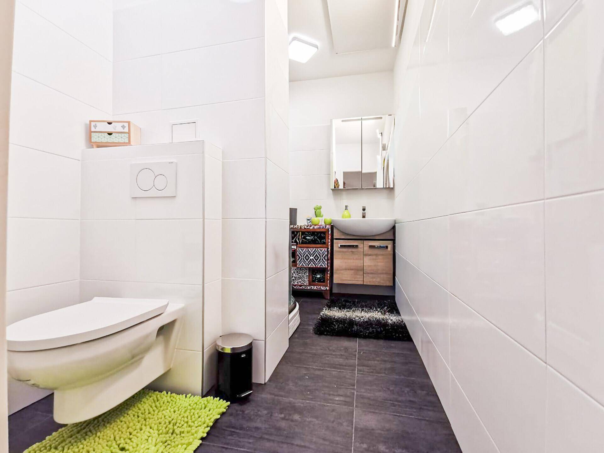 Modern gefliestes Badezimmer mit wandhängendem WC und dunklem Boden.