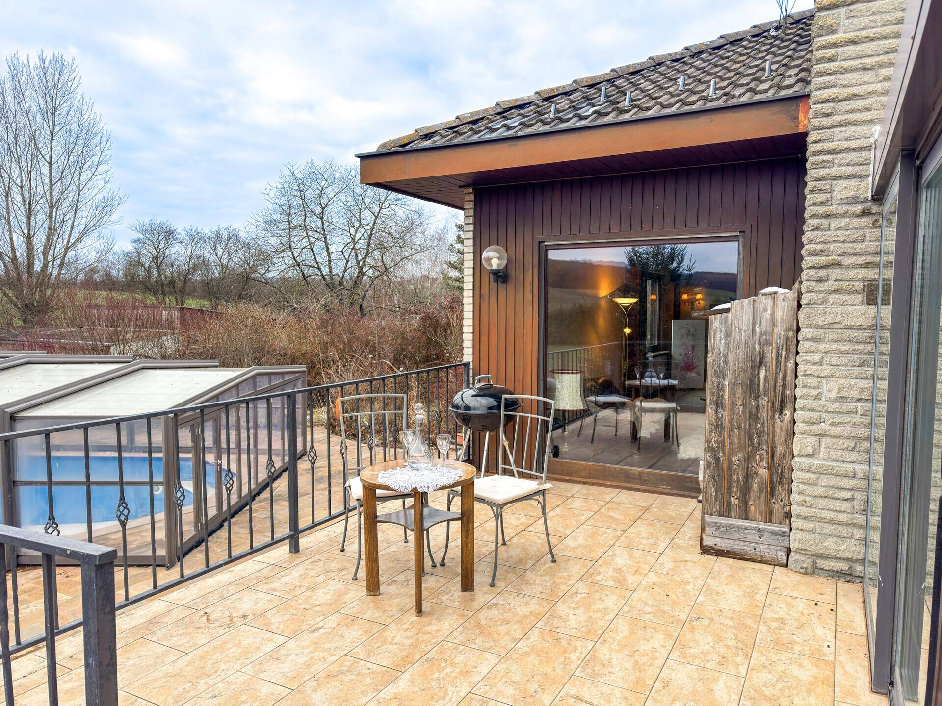 Sonniger Terrassenbereich mit Grill und Sitzgelegenheiten, ideal für Mahlzeiten im Freien mit Blick auf den Pool.