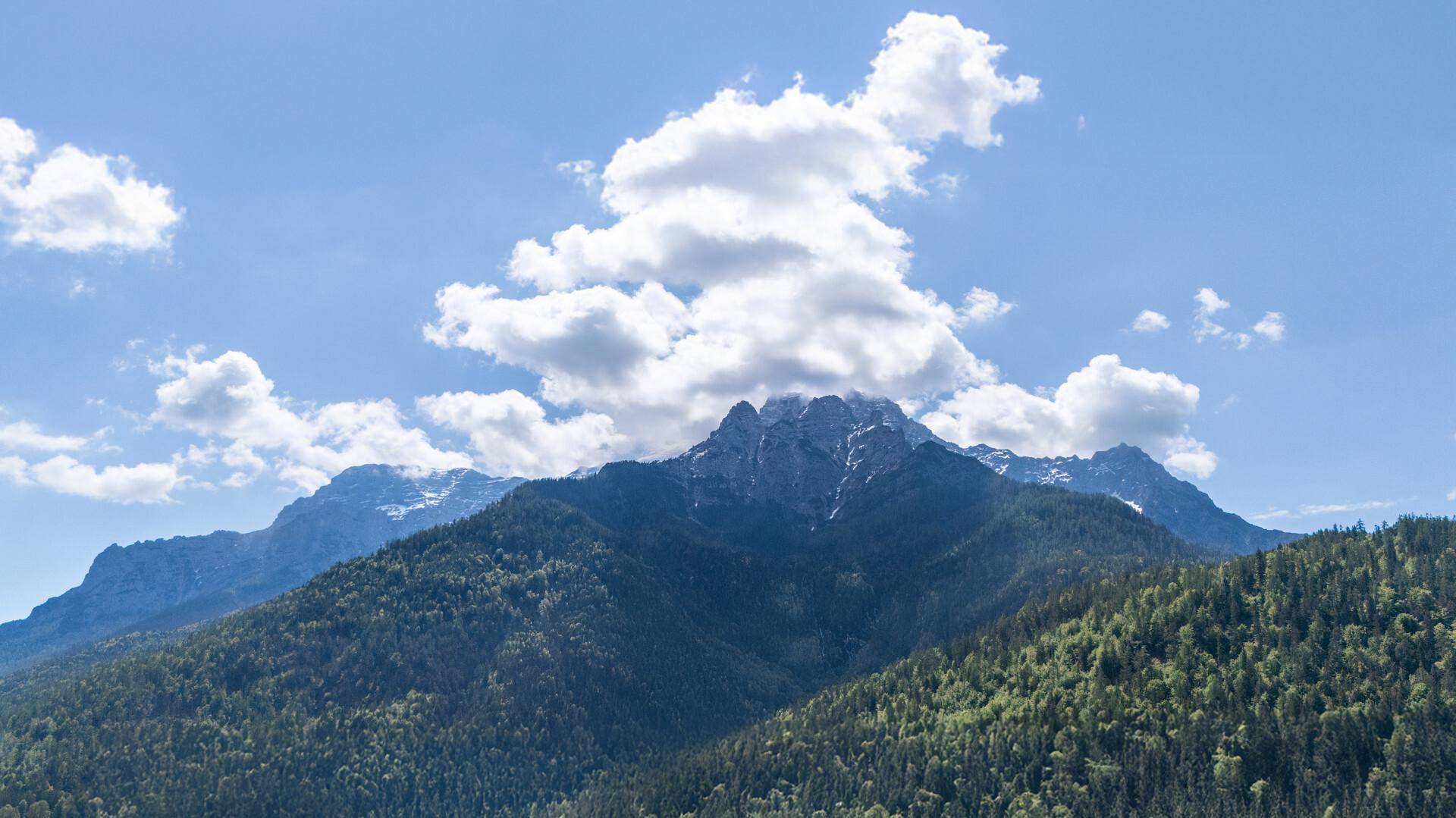 Majestätische, bewaldete Berge unter einem weiten blauen Himmel mit weißen Wolken.