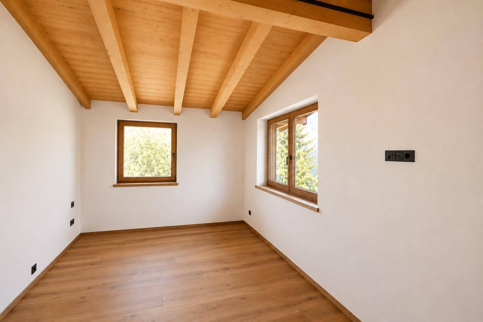 Helles Zimmer mit Holzbalkendecke, Parkettboden und Fenstern mit Blick ins Grüne.