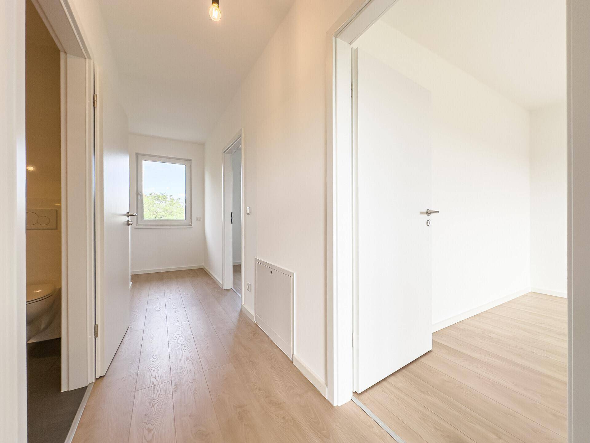 Obergeschoss-Flur mit hellem Holzboden, weißen Wänden und natürlichem Lichteinfall durch ein Fenster.