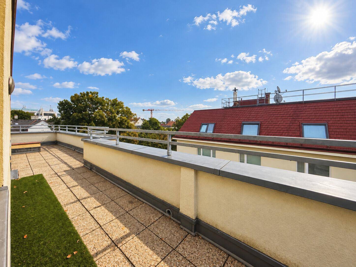 Große Dachterrasse mit Fliesenboden und Kunstrasenbereich unter blauem Himmel.
