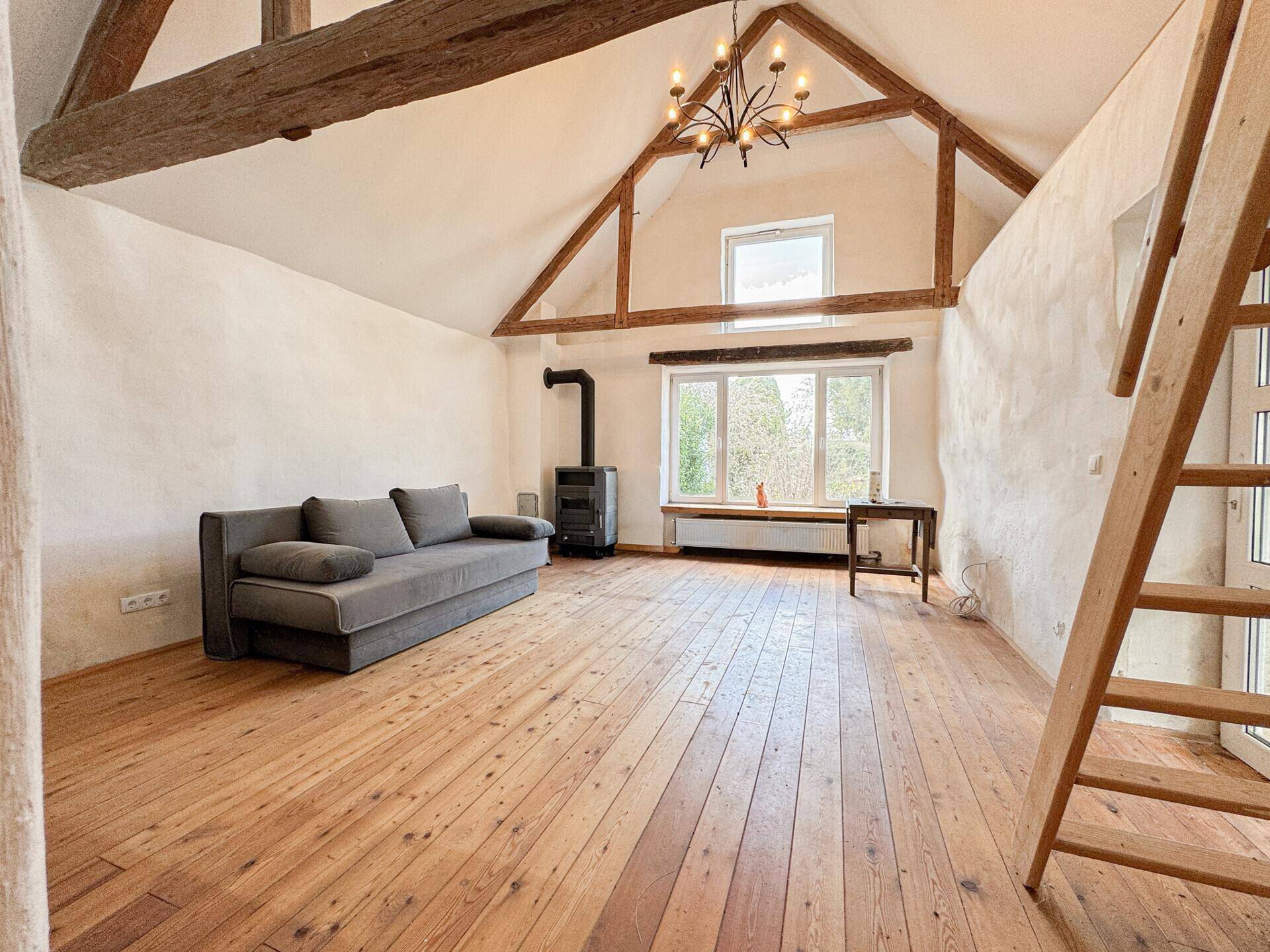 Geräumiges Wohnzimmer mit hohen Decken, Holzbalken und einem gemütlichen Kaminofen.