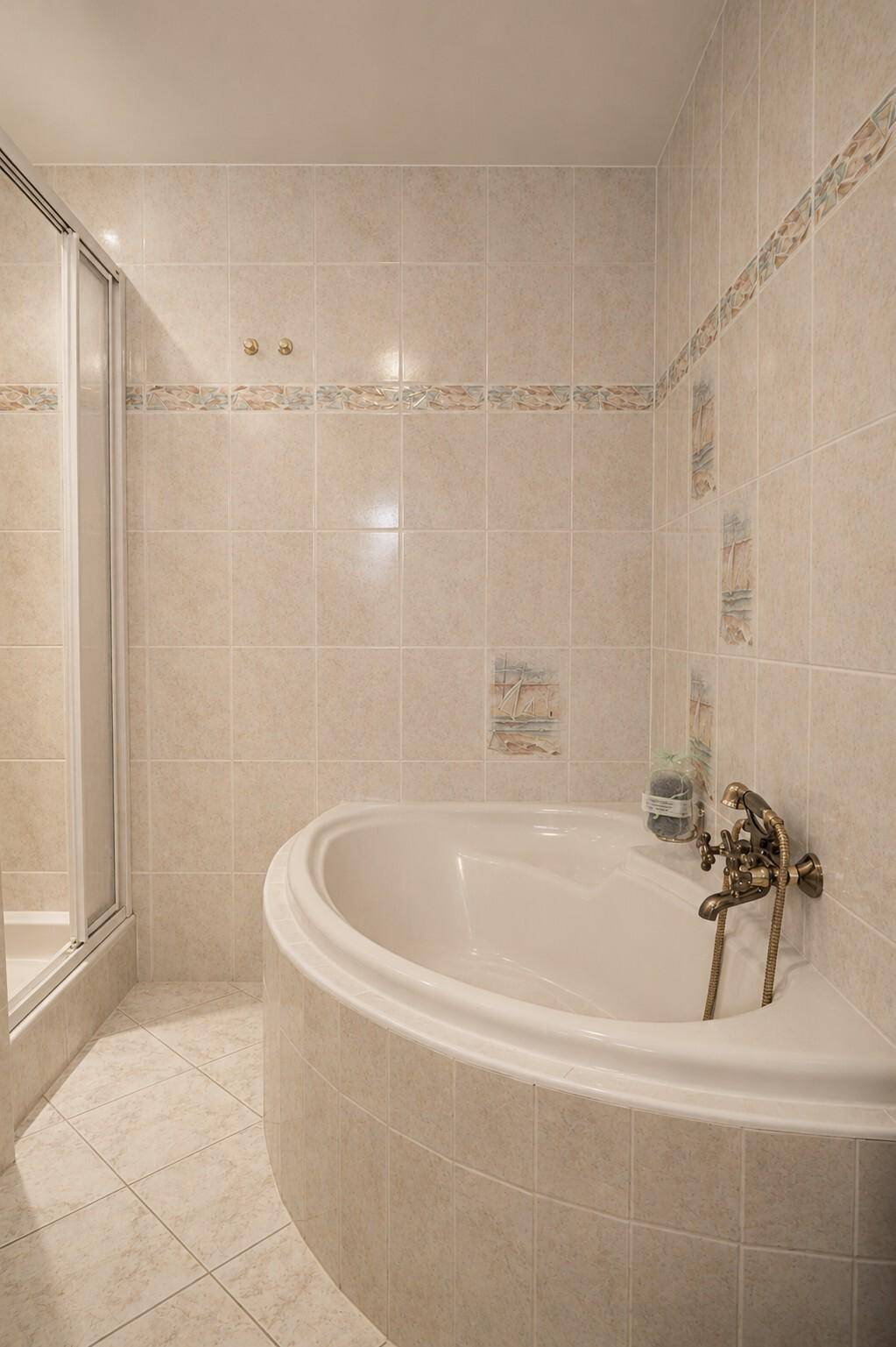 Badezimmer mit Eckbadewanne und beigefarbenen Fliesen, die eine warme Atmosphäre schaffen.