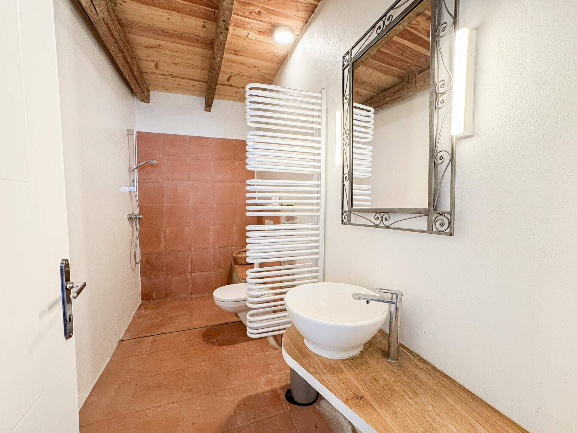 Badezimmer mit Terrakotta-Fliesen, Holzbalkendecke und modernem Waschbecken.