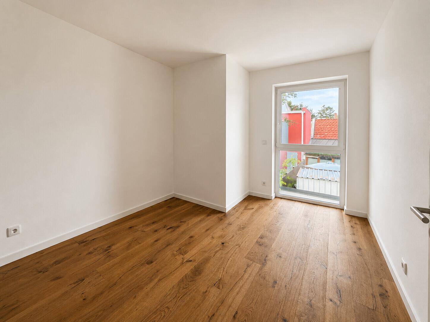 Helles Schlafzimmer mit Holzboden und einem großen Fenster, das viel Licht spendet.