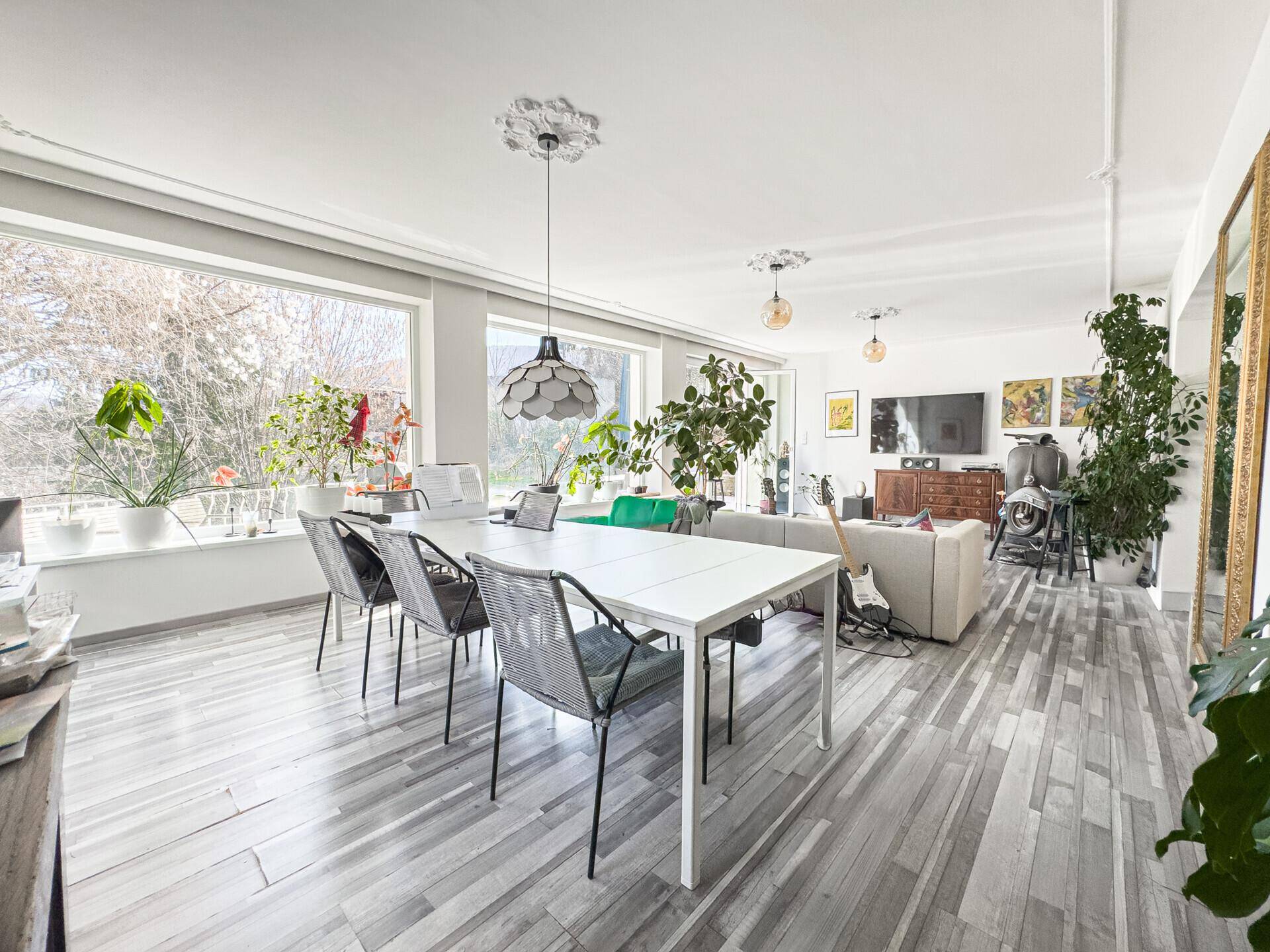 Heller Wohn-Essbereich mit großem Esstisch, bequemer Couch und weitem Ausblick.