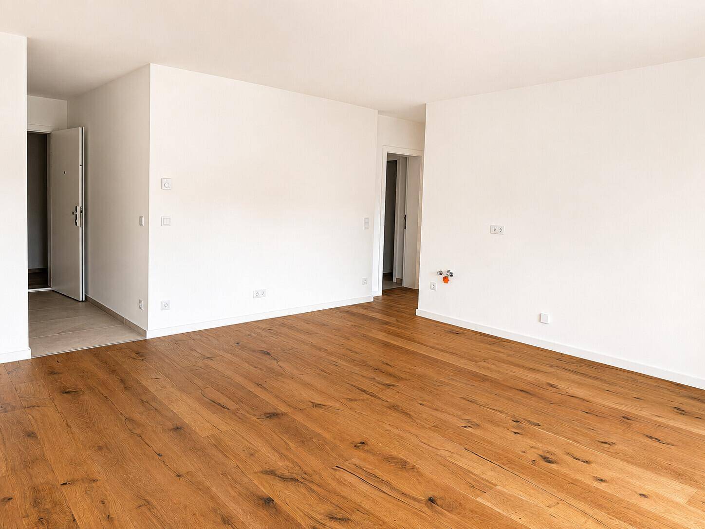 Offener Innenraum mit Holzboden und weißen Wänden, der zu weiteren Zimmern führt.