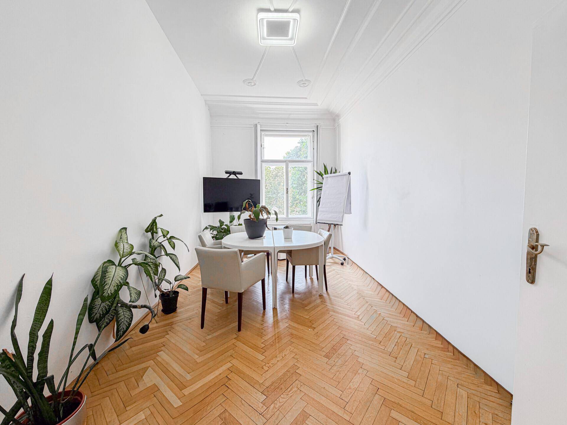 Helles Büro mit Fischgrätparkett, rundem Tisch und Pflanzen, ideal für Besprechungen.