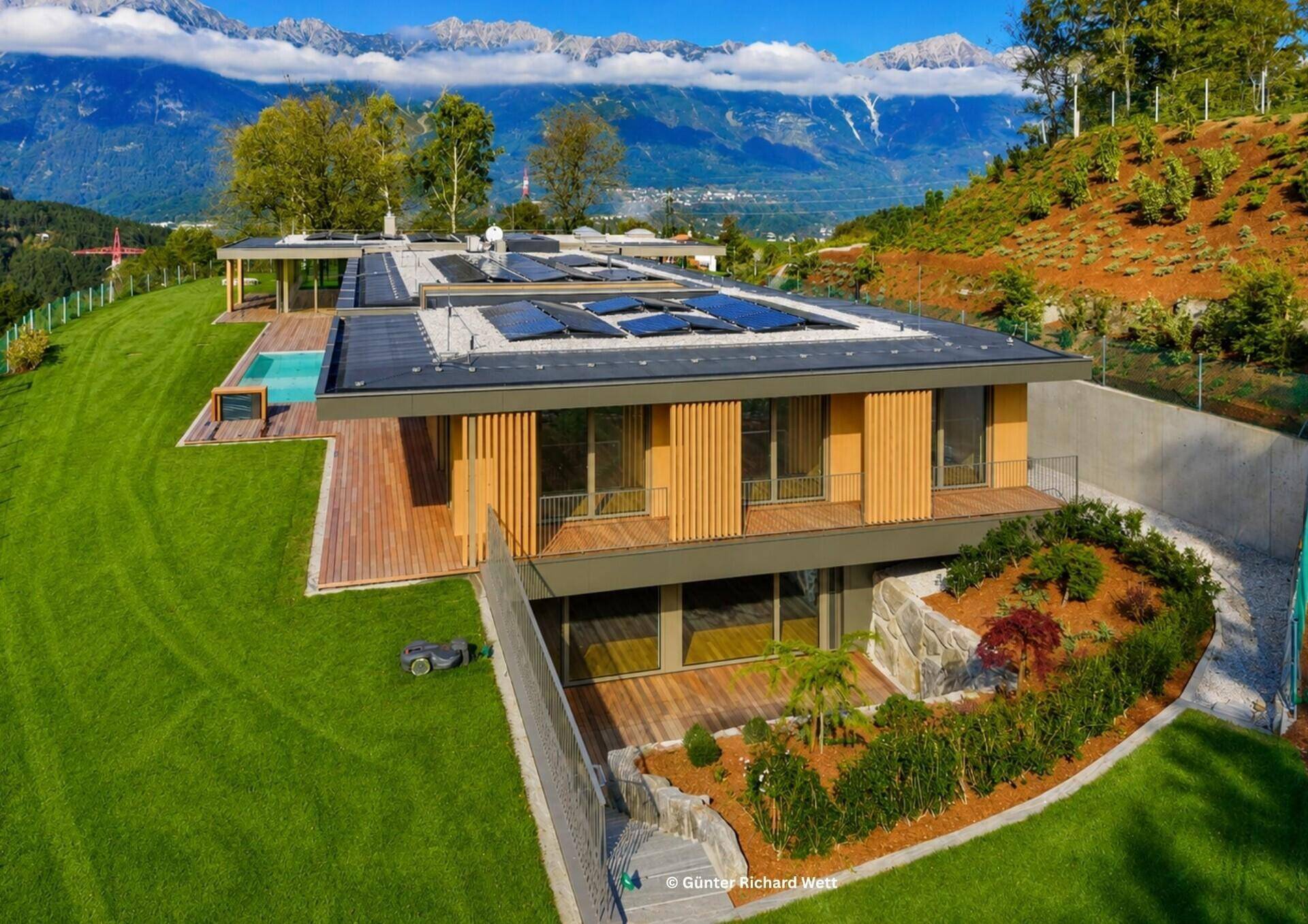 Moderne Villa in Hanglage mit Pool, Solaranlage und weitläufigem Garten vor beeindruckender Bergkulisse.