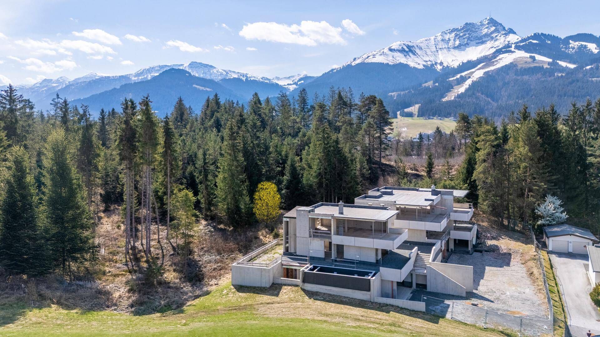 Luftaufnahme eines im Bau befindlichen Gebäudes in alpiner Landschaft mit schneebedeckten Bergen.