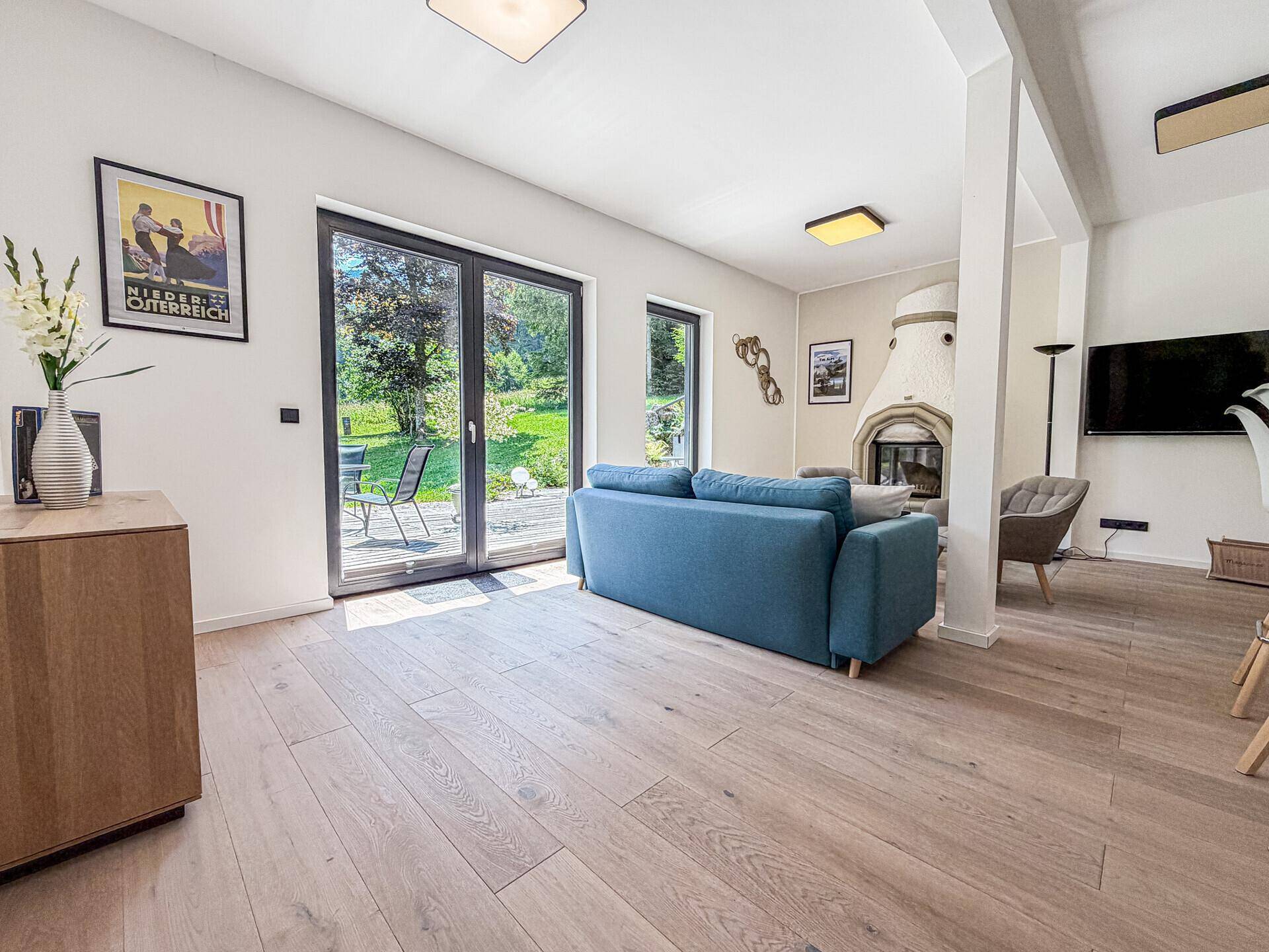 Gemütliches Wohnzimmer mit blauem Sofa, Holzboden und direktem Zugang zur Außenterrasse.