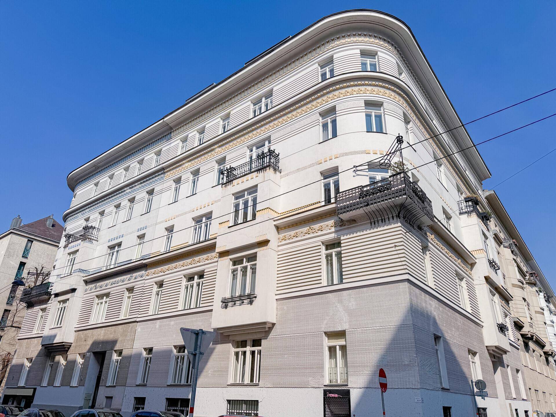Historische Gebäudefassade mit eleganten Verzierungen, Balkonen und großen Fenstern unter blauem Himmel.