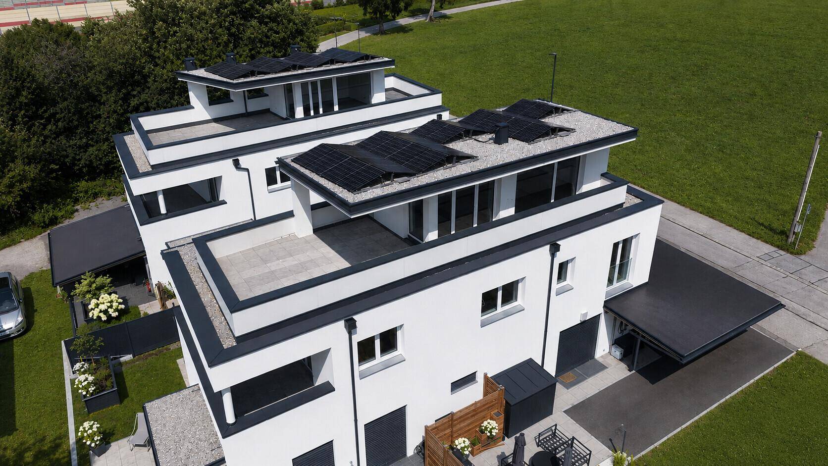 Luftaufnahme von modernen Reihenhäusern mit Solaranlagen auf den Flachdächern und grüner Umgebung.