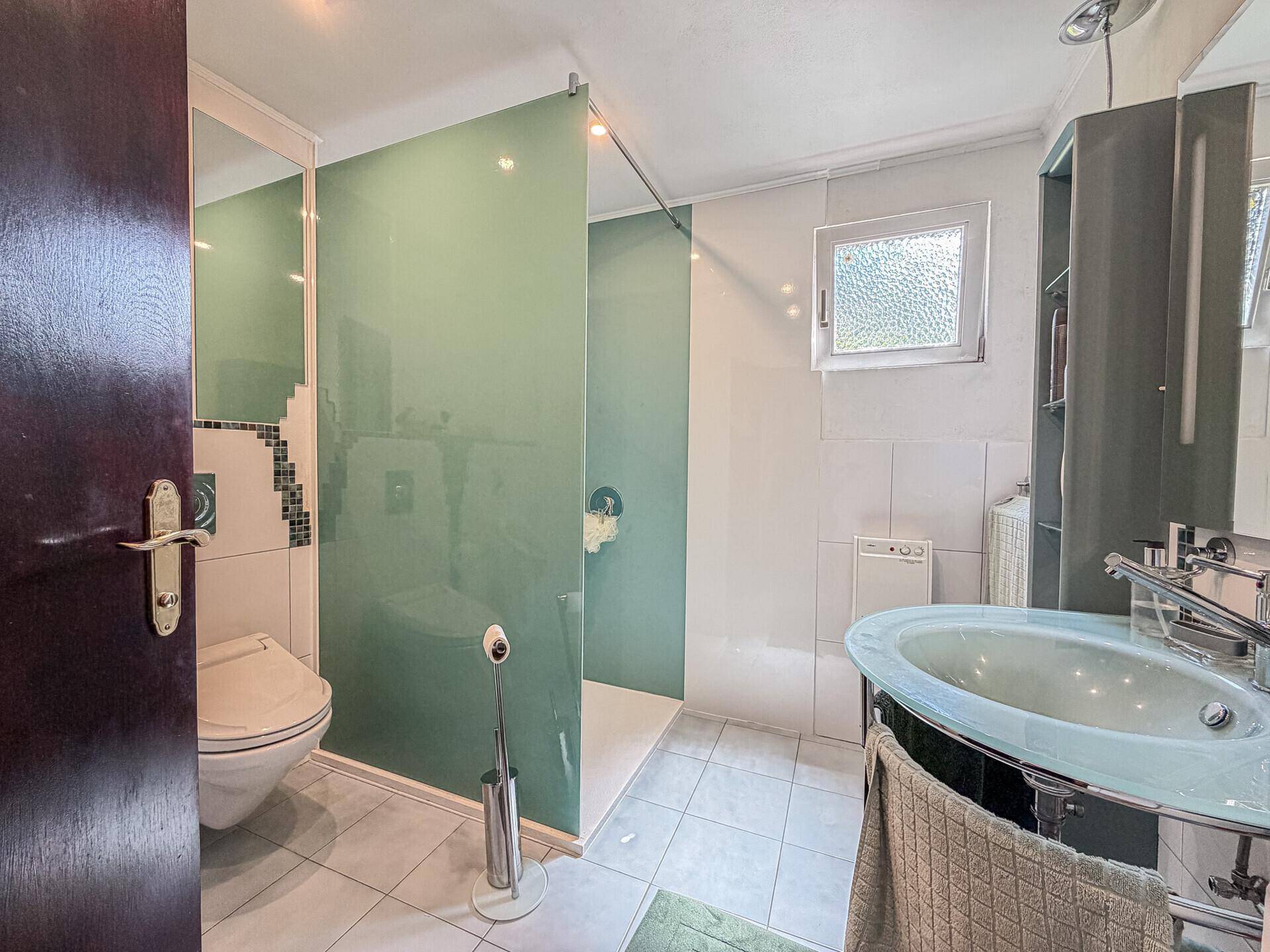 Modernes Badezimmer mit begehbarer Dusche, WC und Fenster.
