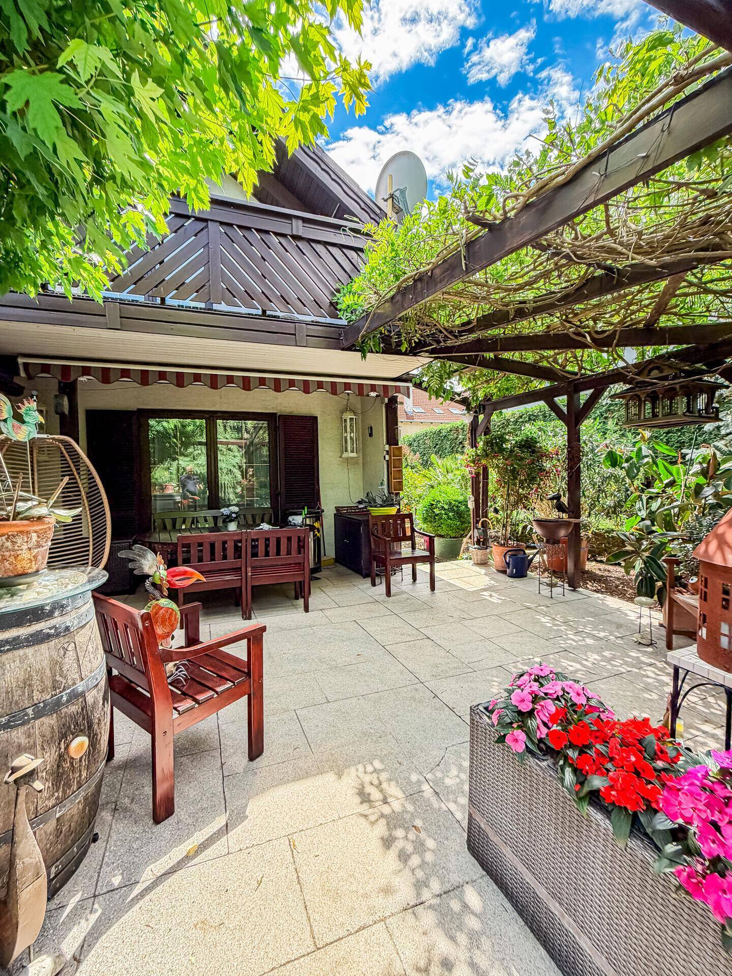 Gemütliche Terrasse mit Blumenkästen und Holzmöbeln unter einer bewachsenen Pergola.
