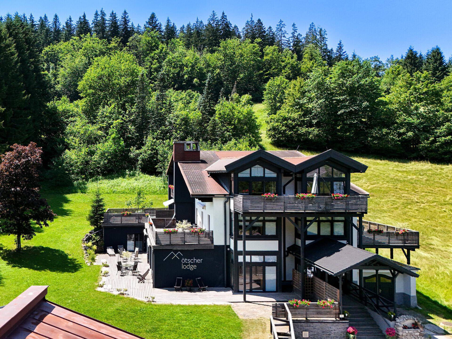 Modernes Gebäude im alpinen Stil, eingebettet in eine grüne Landschaft mit Wäldern und Wiesen.