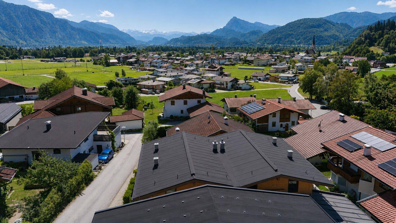 Weitläufige Luftaufnahme einer Wohnsiedlung mit Häusern und Bergen im Hintergrund unter blauem Himmel.
