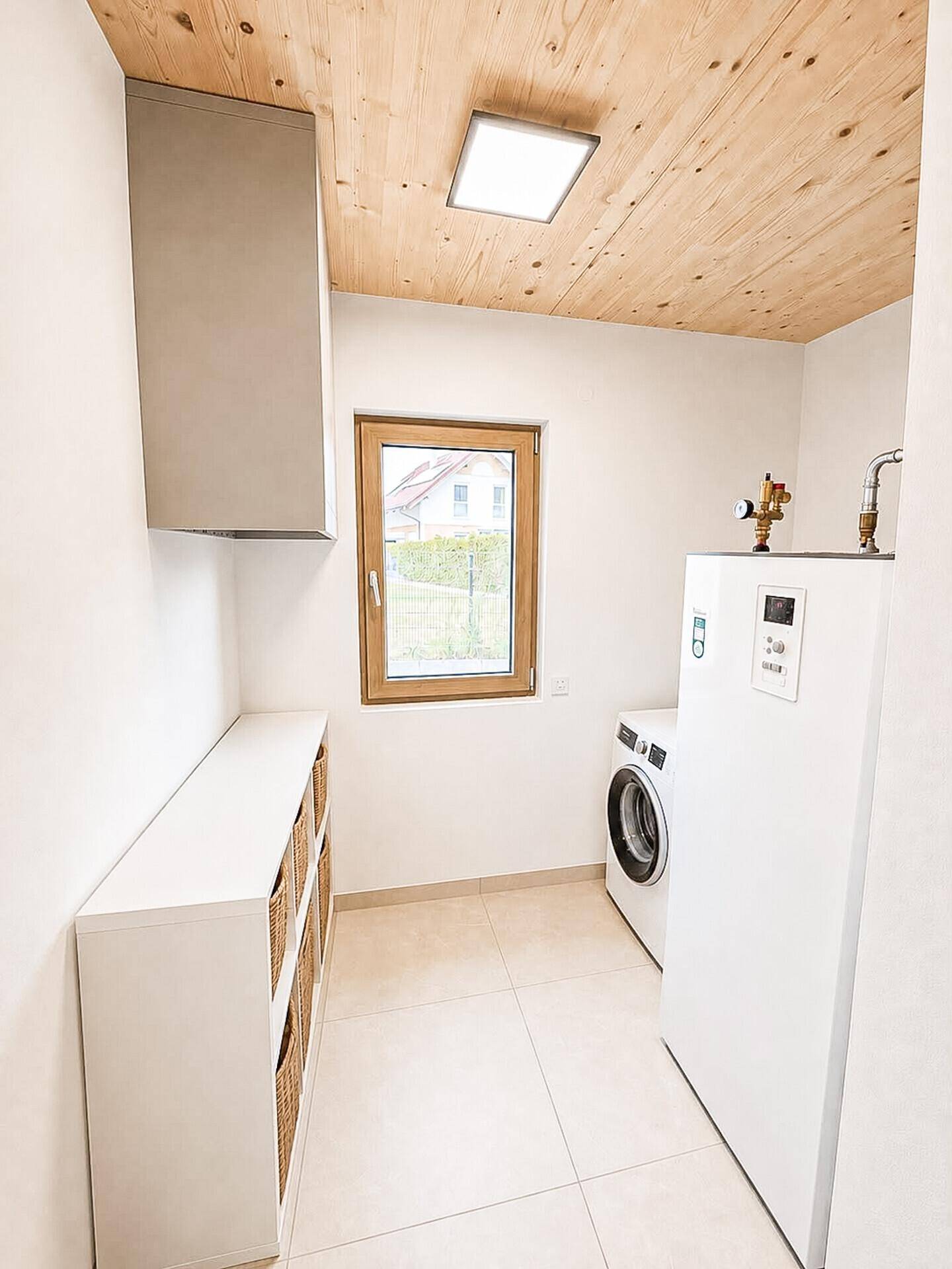 Praktischer Hauswirtschaftsraum mit Waschmaschine, Wärmepumpe und Fenster, ausgestattet mit Fliesenboden.