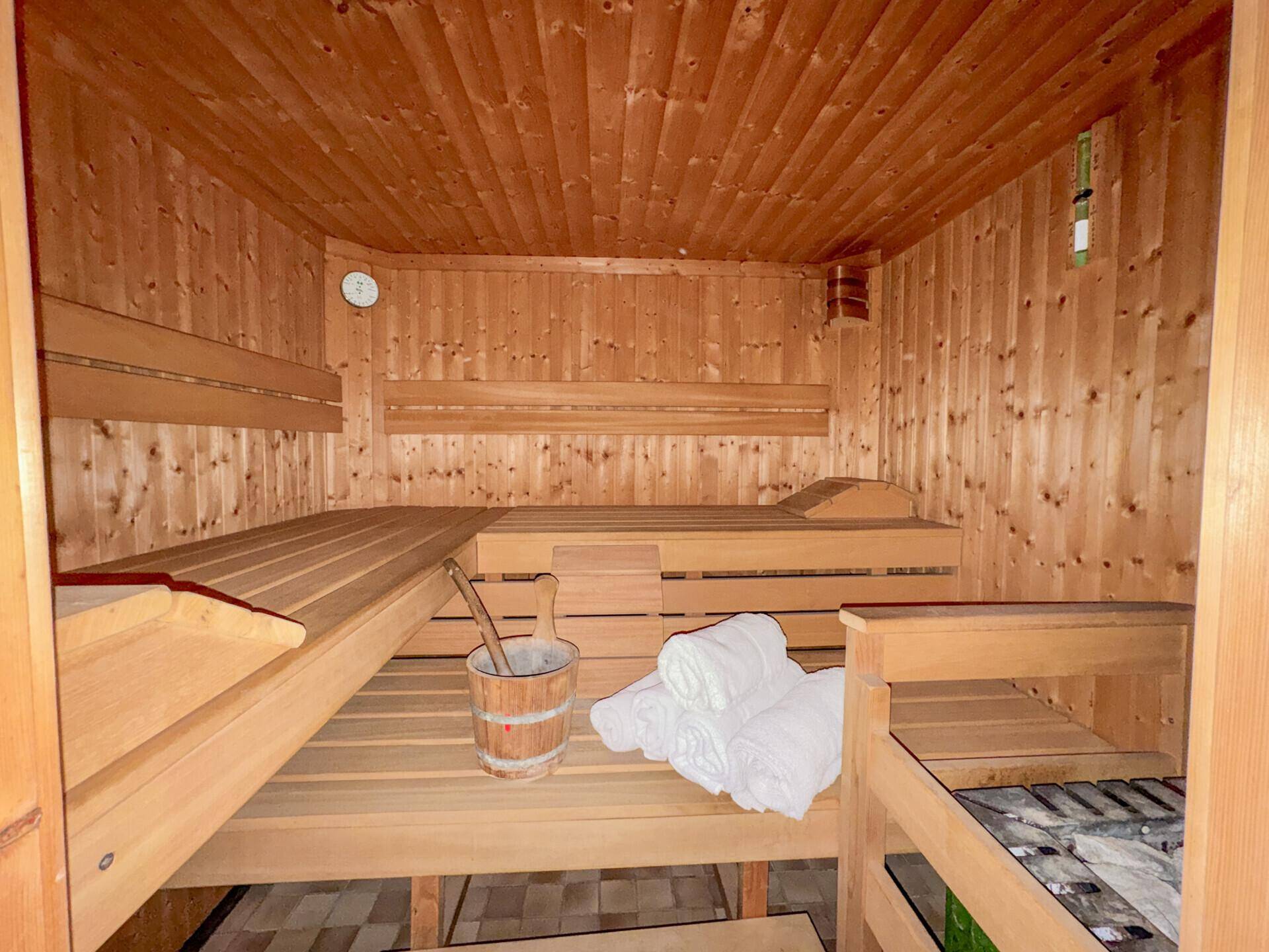 Traditionelle Holzsauna mit Bänken und Eimer für entspannende Wellnessmomente im eigenen Zuhause.