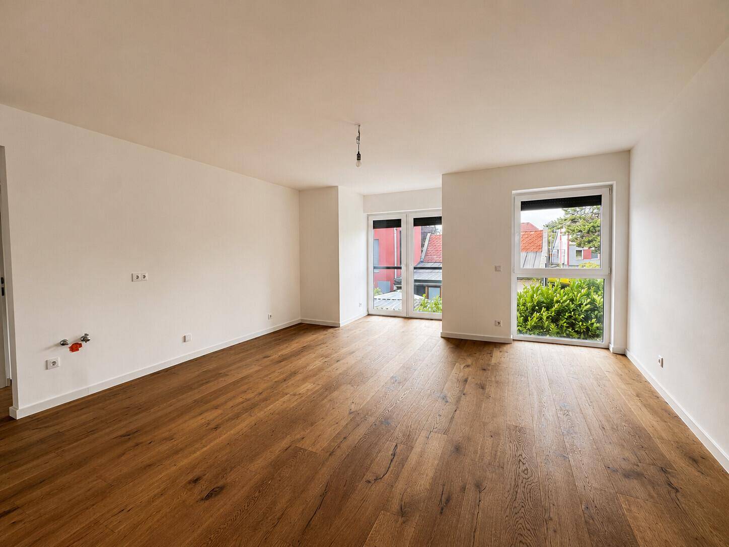 Geräumiges, unmöbliertes Zimmer mit hellem Holzboden und Zugang zu einem Außenbereich.