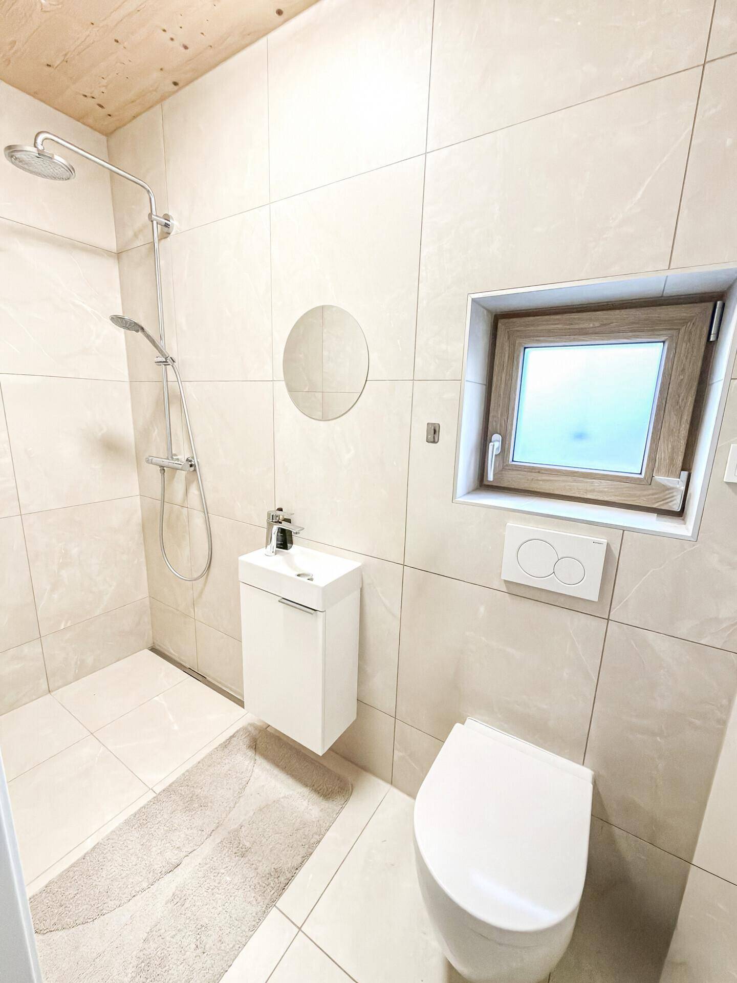 Modernes Badezimmer mit begehbarer Dusche, Wand-WC und kleinem Waschbecken, hell gefliest und funktional.