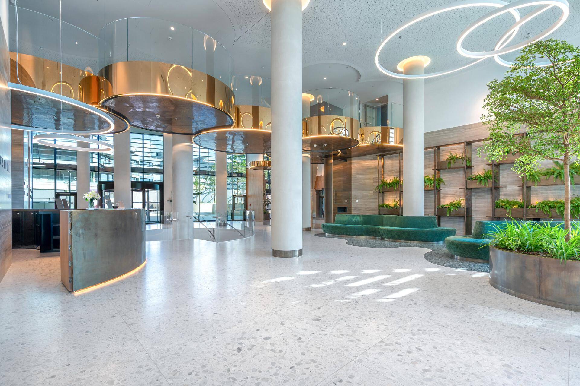 Luxuriöse und moderne Lobby mit hohen Decken, stilvoller Beleuchtung, Rezeption und Grünpflanzen.