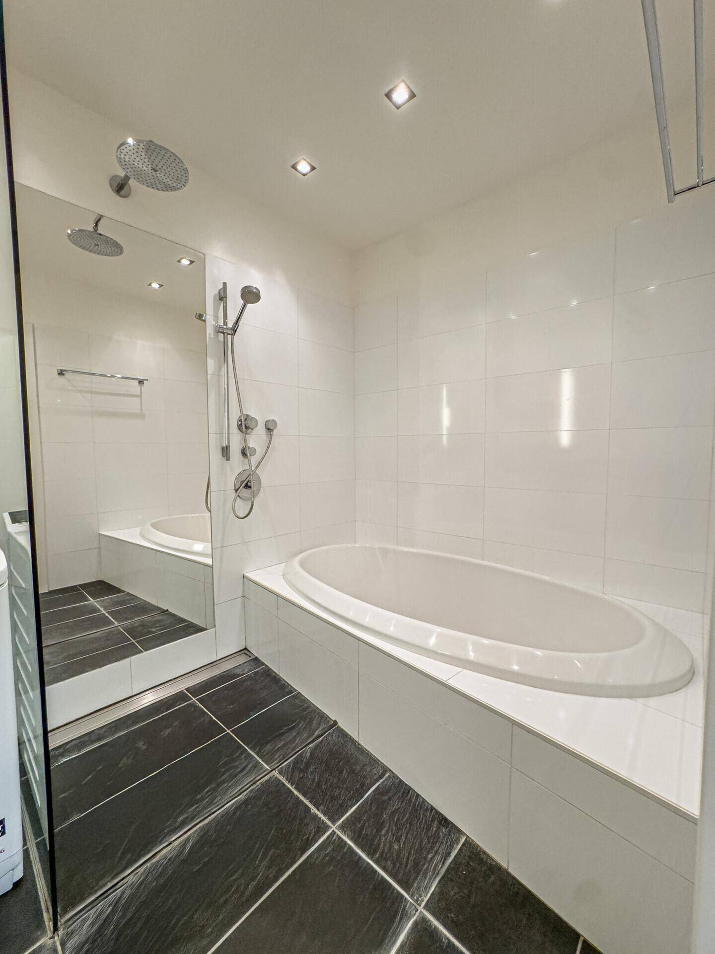 Modernes Badezimmer mit großer Badewanne, Regendusche und dunklen Bodenfliesen.