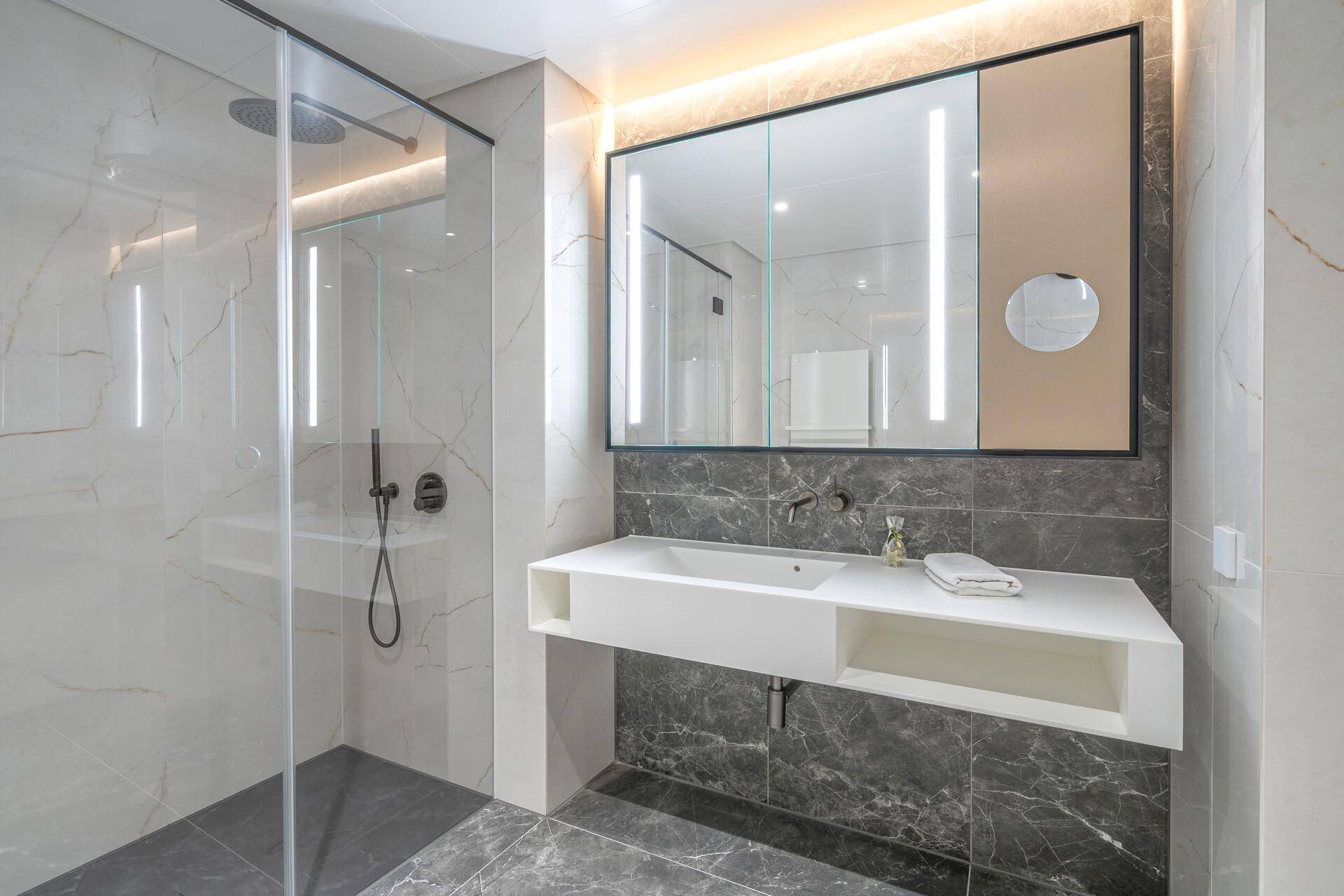 Modernes Badezimmer mit begehbarer Dusche, eleganten Marmorfliesen und einem stilvollen Waschtisch mit Spiegelschrank.