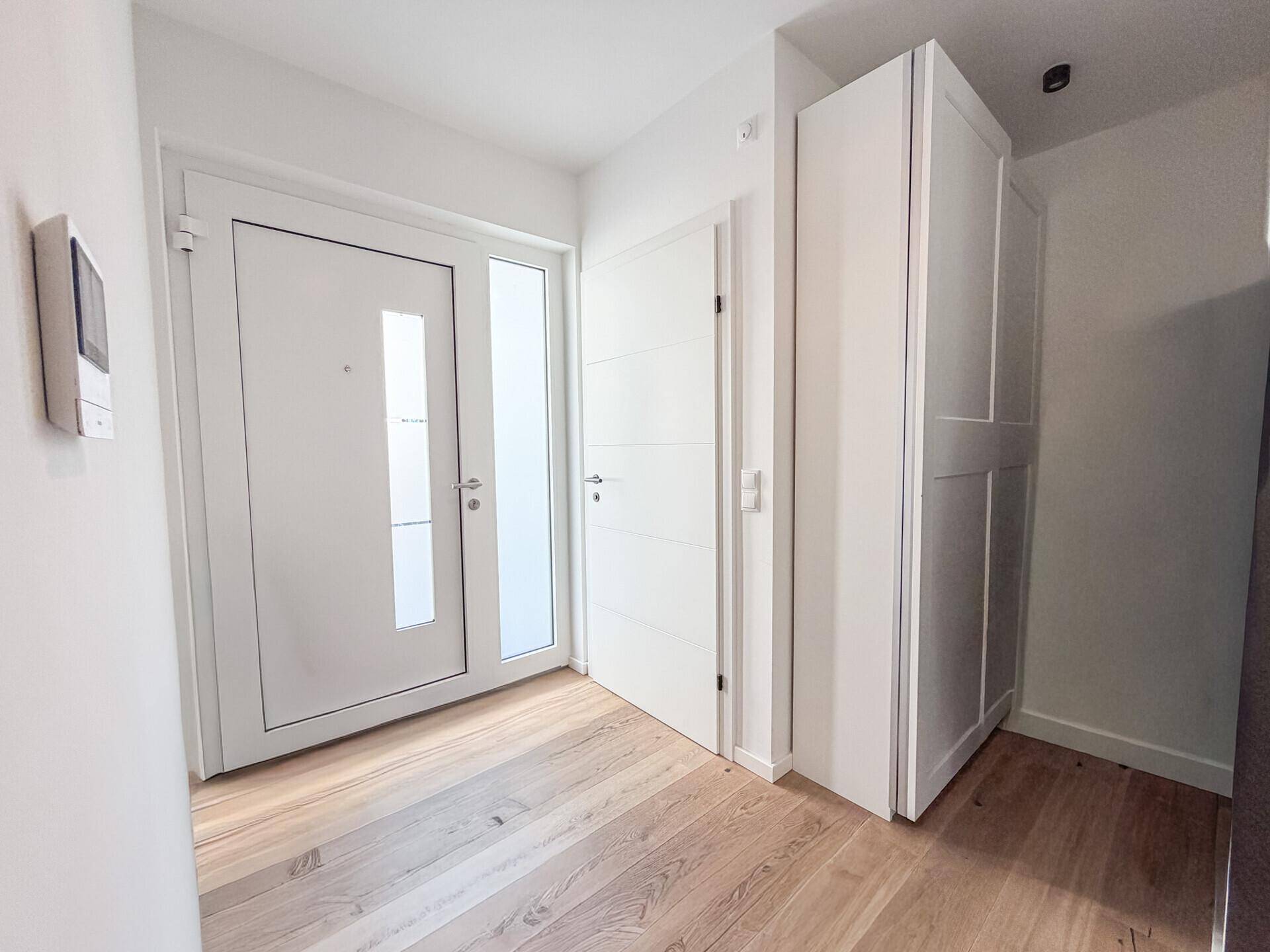 Heller Eingangsbereich mit Holzboden und weißer Garderobe.