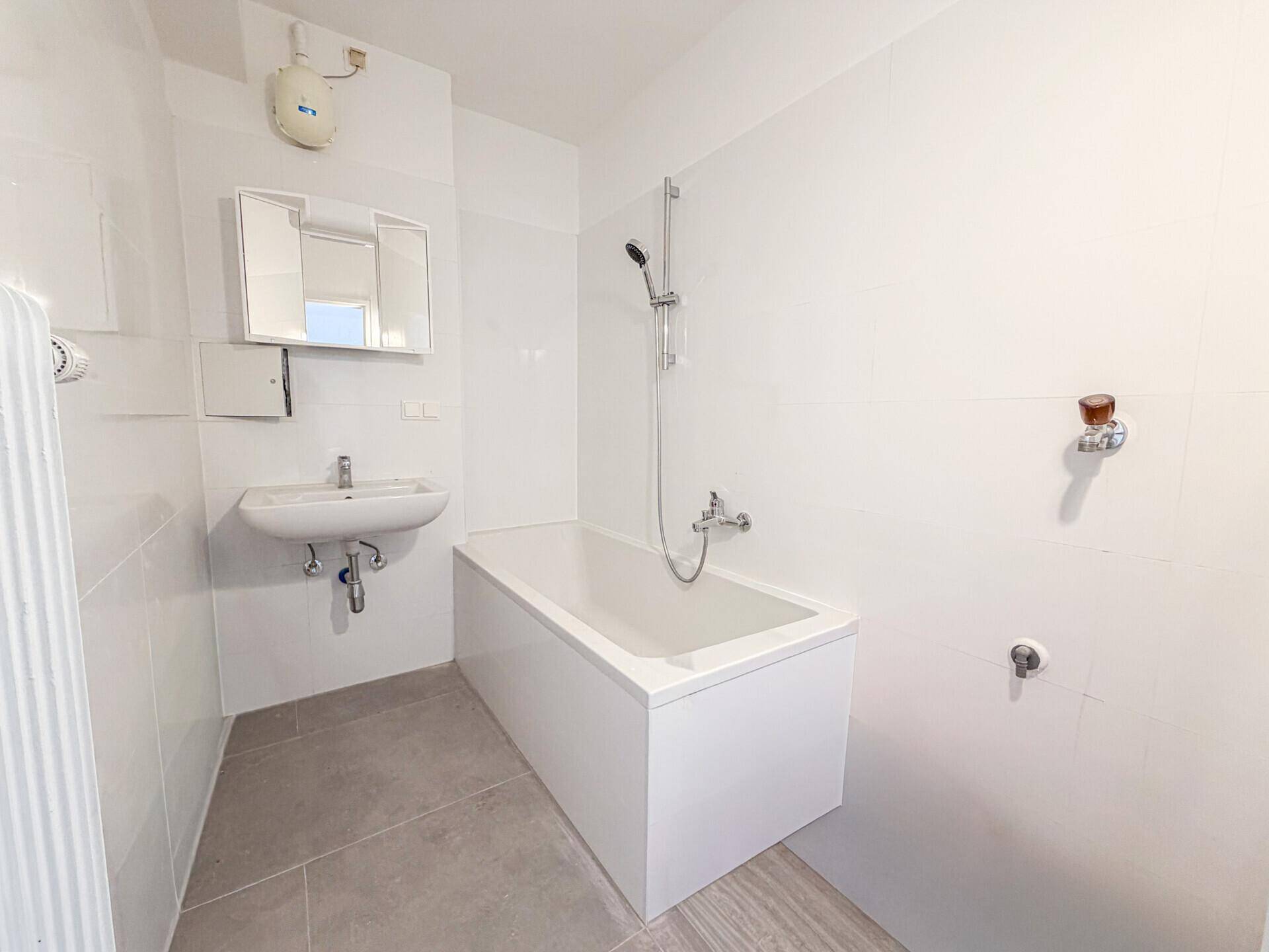 Modern gefliestes Badezimmer mit Badewanne, Duschfunktion und Waschbecken mit Spiegelschrank.