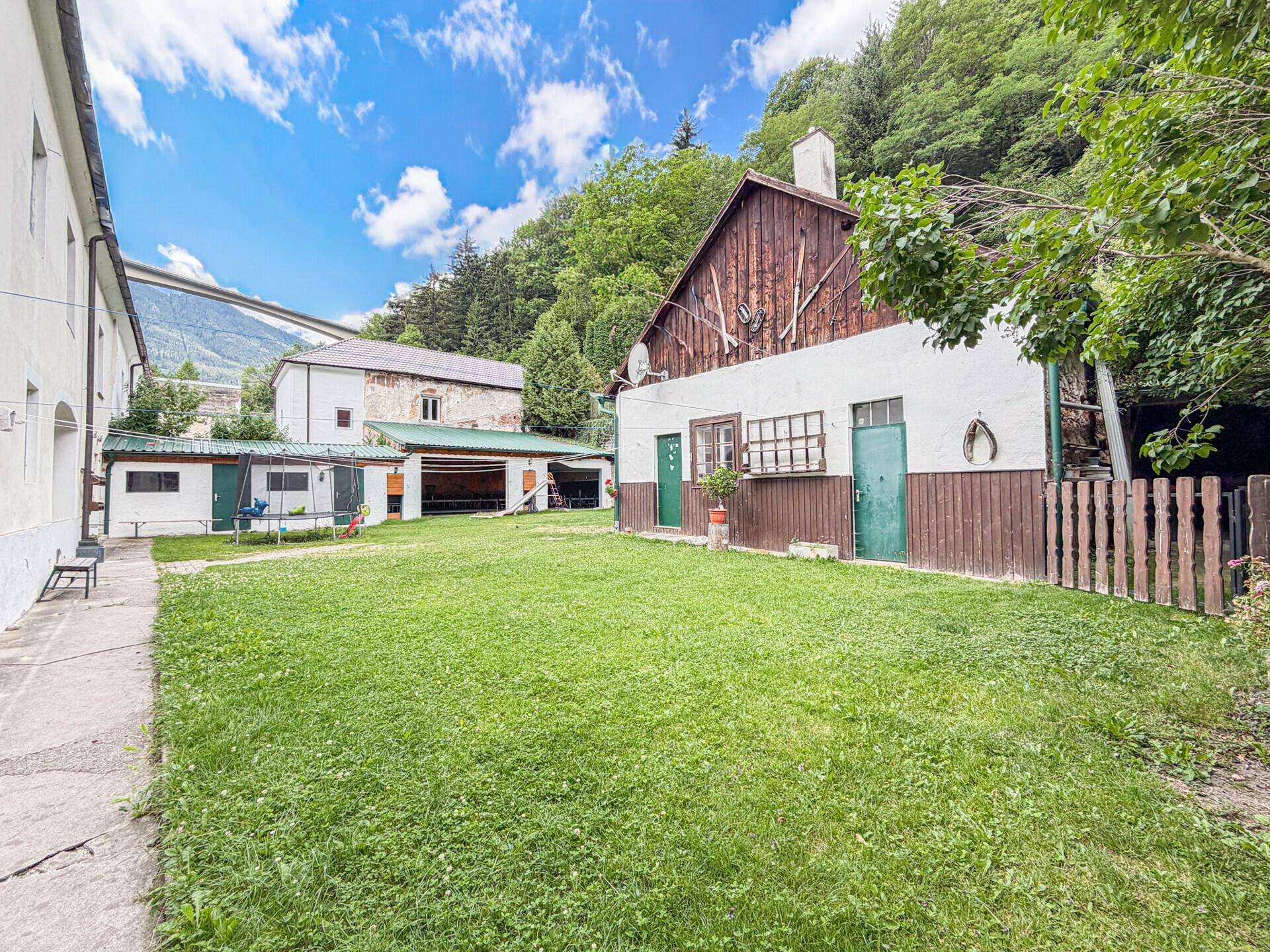 Großer grüner Gartenbereich mit Rasenfläche und einem rustikalen Holzhaus im Hintergrund.