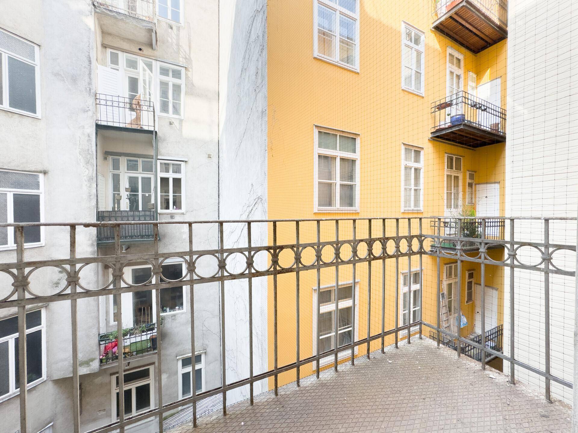 Blick vom Balkon in einen Innenhof zwischen Gebäuden mit unterschiedlichen Fassadenfarben.