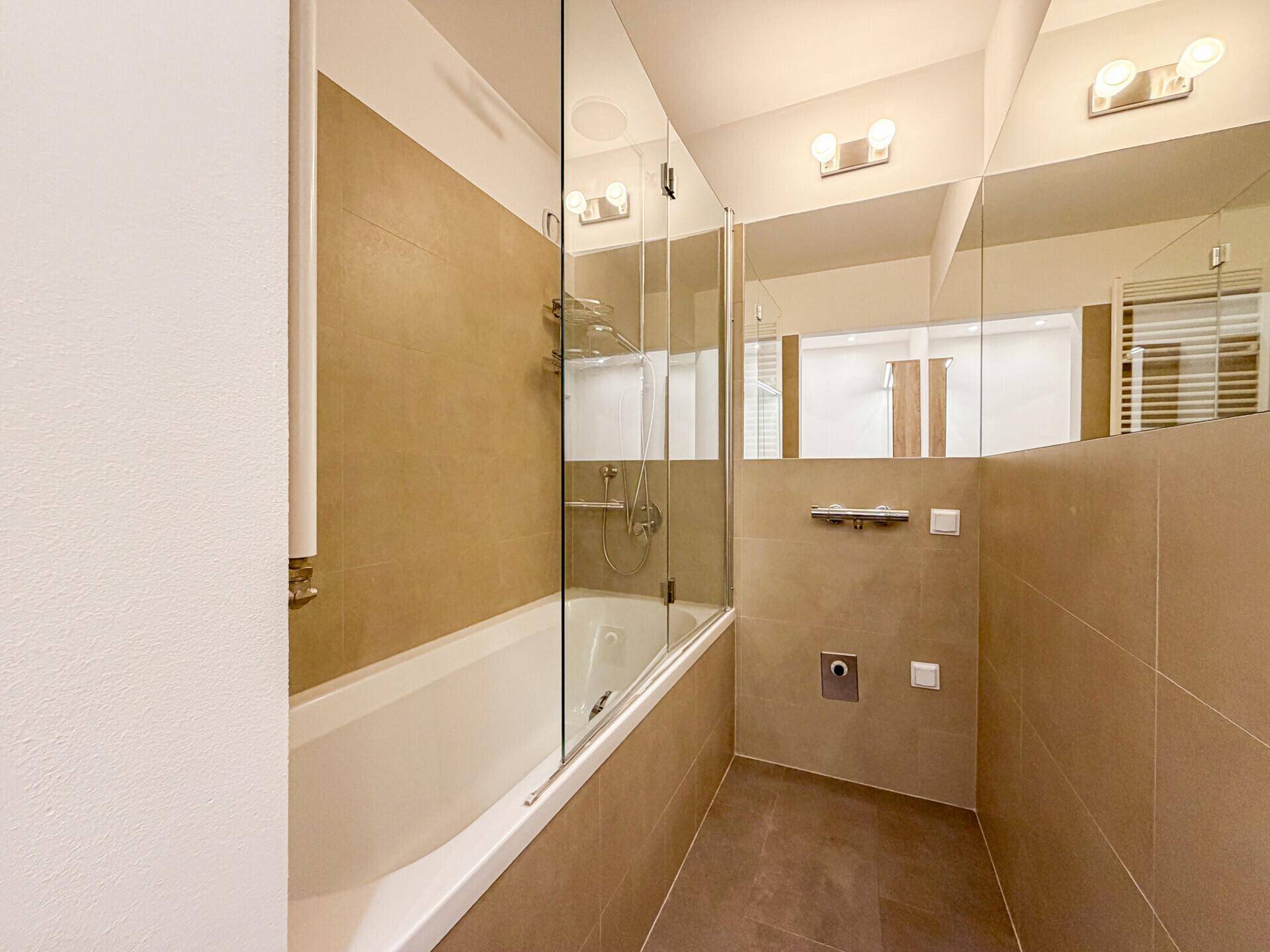 Modernes Badezimmer mit Badewanne, Duschabtrennung aus Glas und beigefarbenen Fliesen.