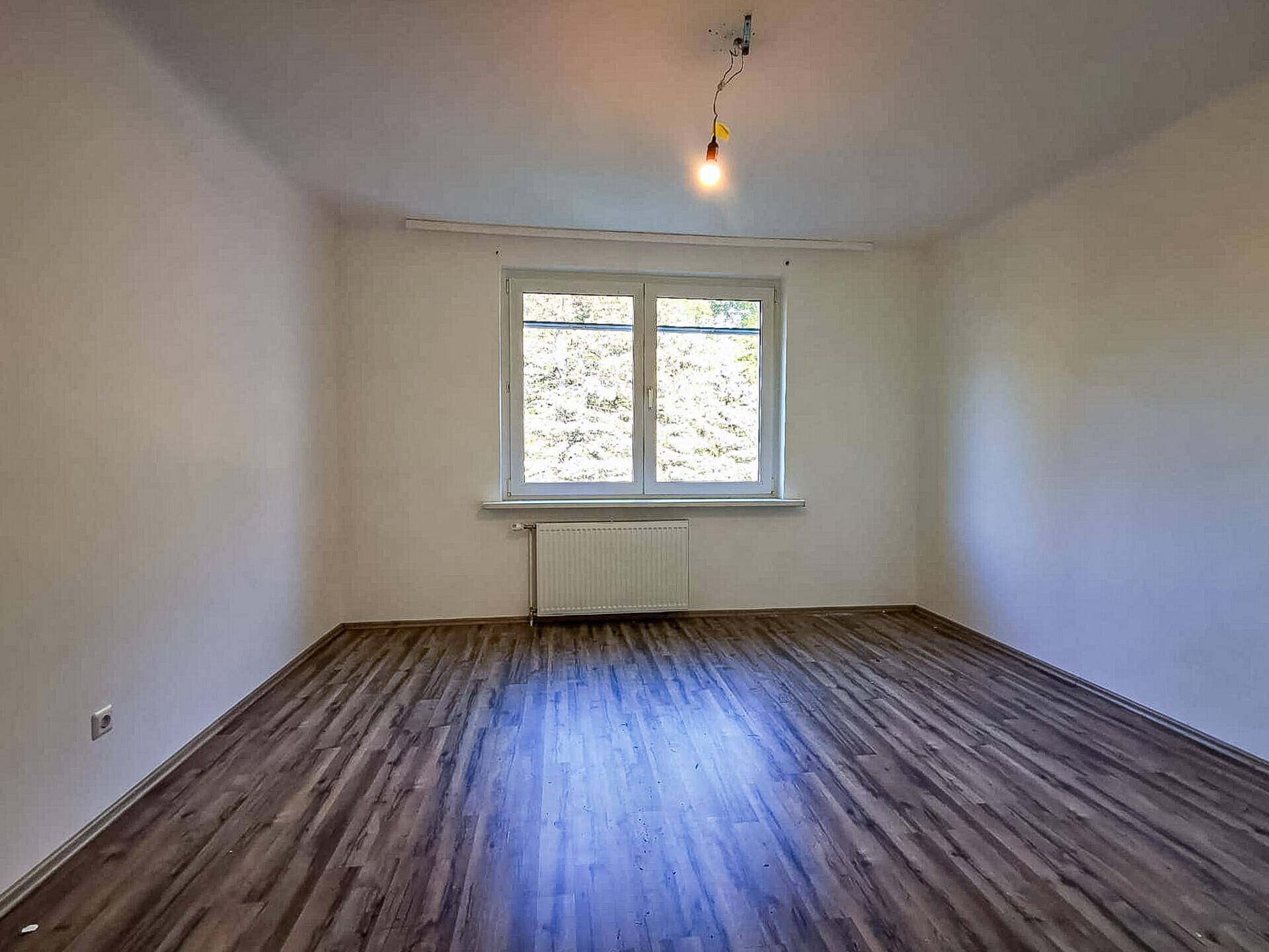 Helles Zimmer mit Laminatboden, weiß gestrichenen Wänden und einem großen Fenster.