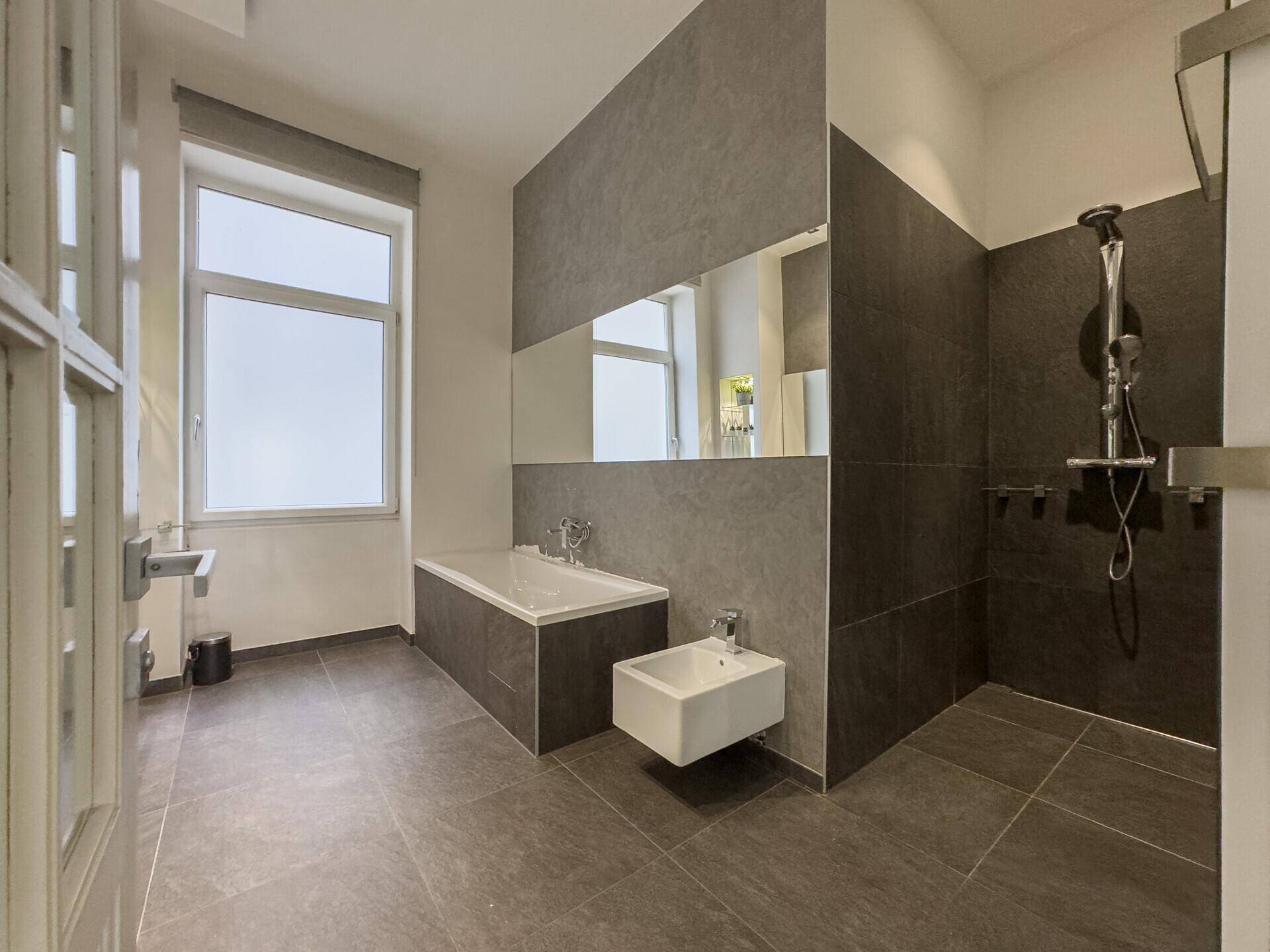 Modernes Badezimmer mit großer Badewanne, separater Dusche und Bidet, alles in dunklen Fliesen gehalten.