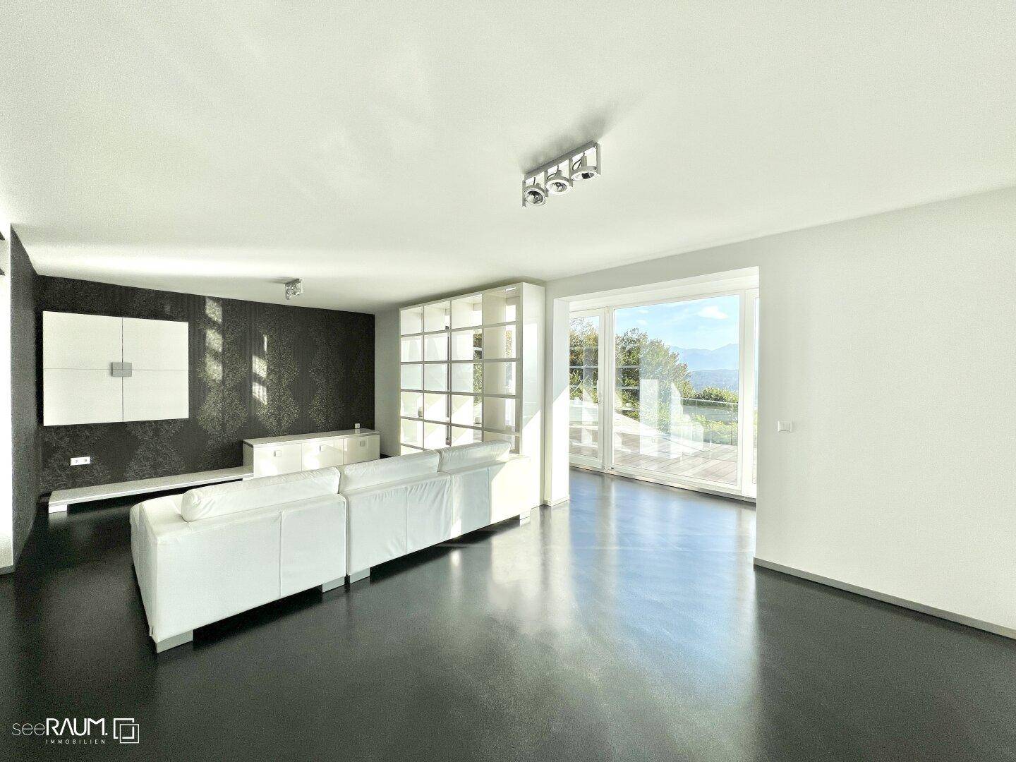 Helles Wohnzimmer mit moderner Einrichtung, dunkler Akzentwand und großen Fenstern mit Panoramablick.