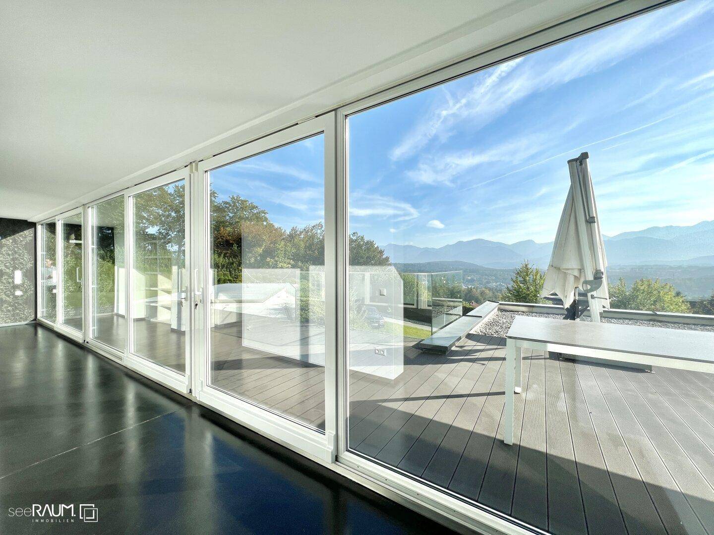 Lichtdurchfluteter Innenraum mit raumhohen Fenstern, die einen weiten Blick auf die Berge und die Terrasse bieten.