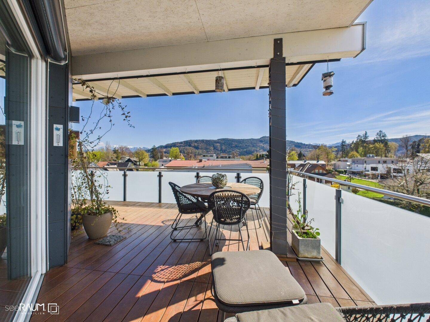Helle Terrasse mit Holzboden, Esstisch und Panoramablick auf die umliegende Landschaft und Berge.