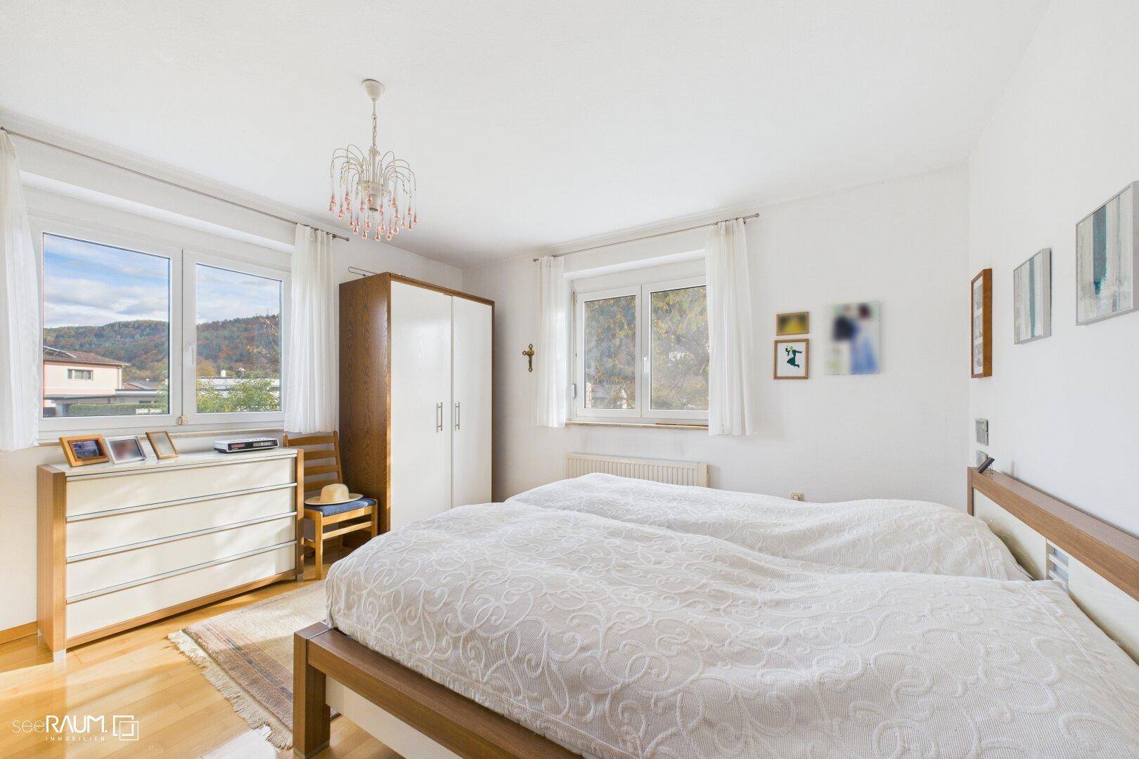 Helles Schlafzimmer mit zwei Betten, Kommode und einem schönen Blick ins Grüne durch die Fenster.