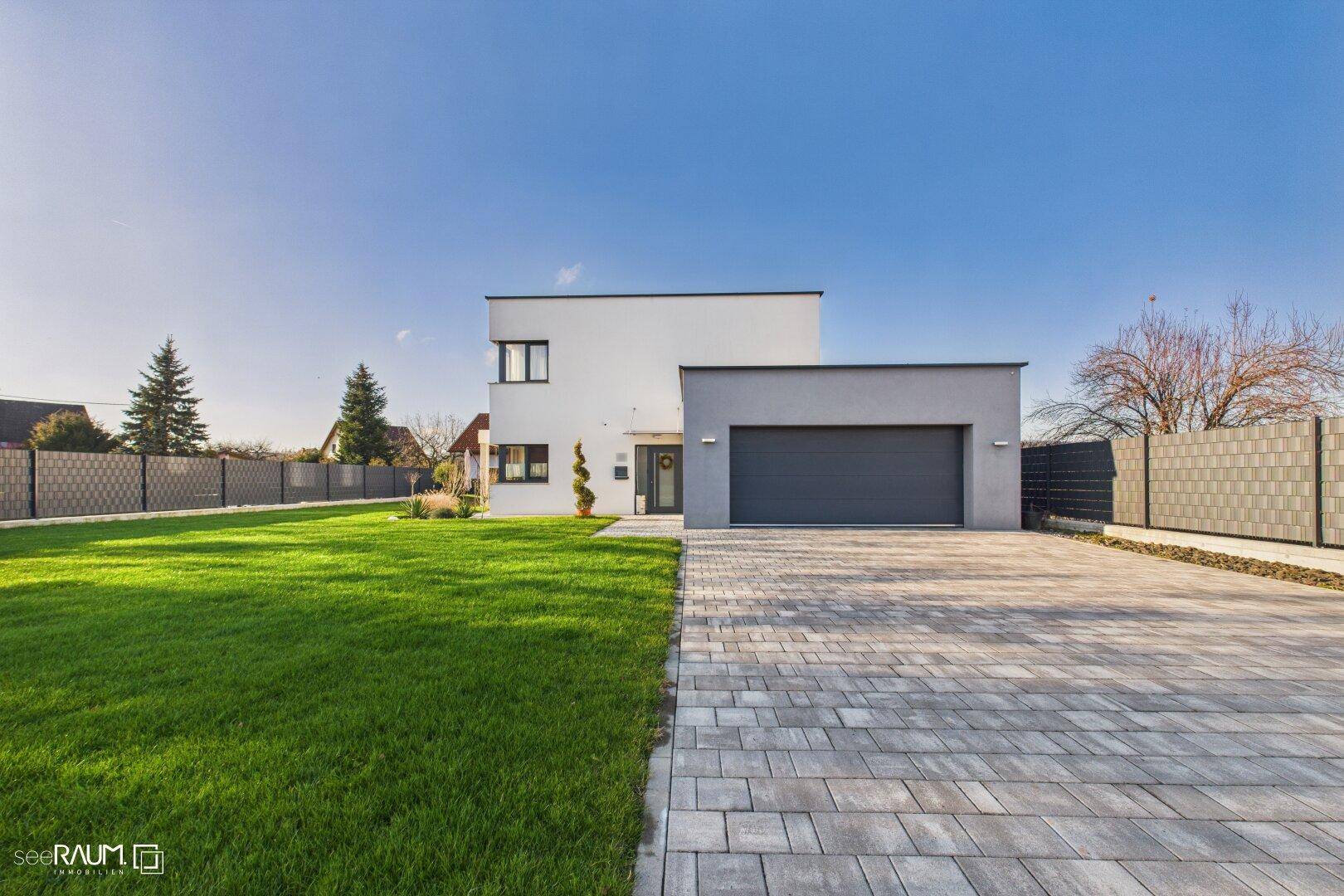 Moderne Einfamilienhausfassade mit integrierter Garage, gepflegtem Rasen und großer Auffahrt.