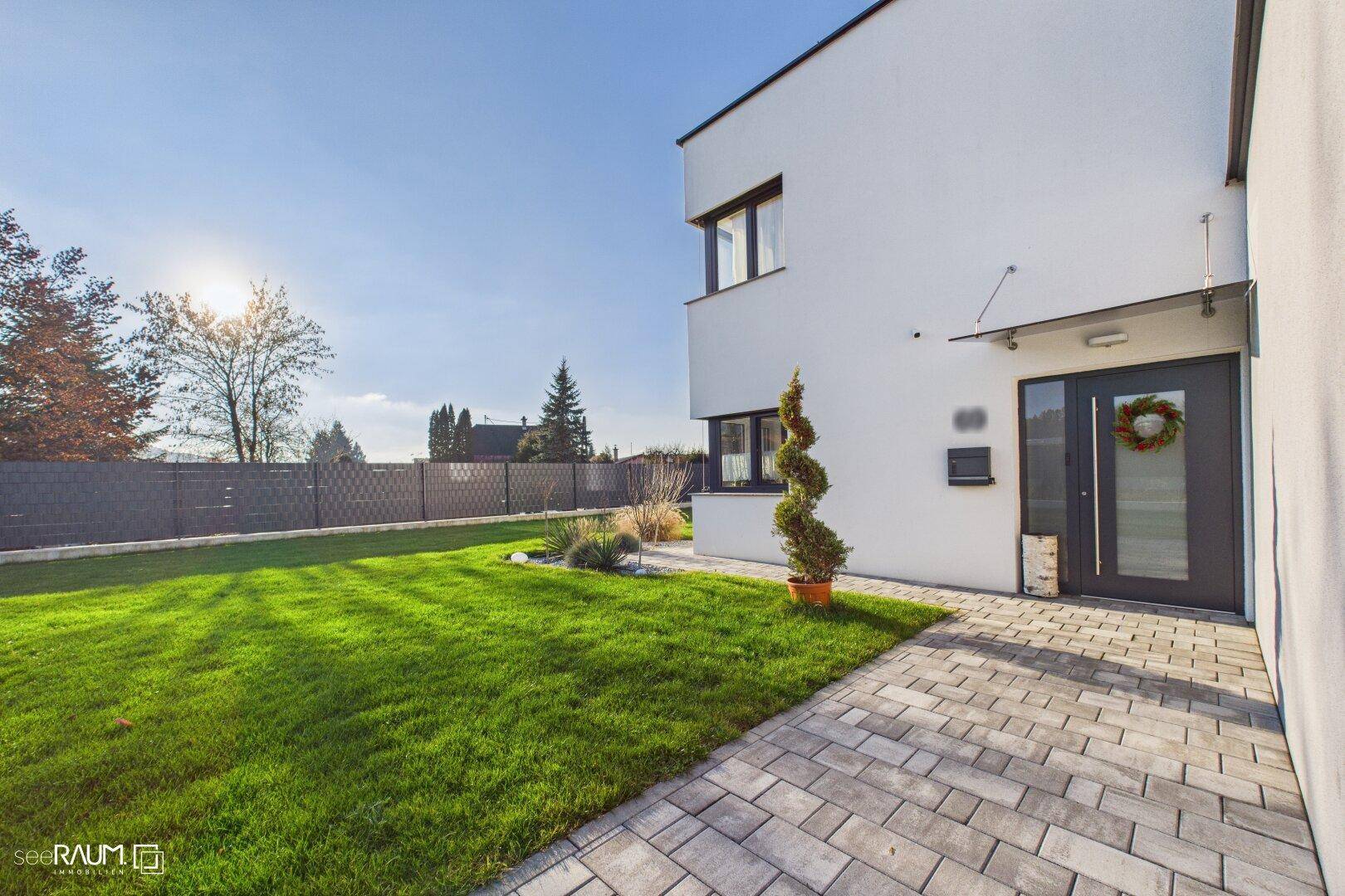 Eingangsbereich des modernen Hauses mit gepflastertem Weg, Rasenfläche und sonniger Ausrichtung.