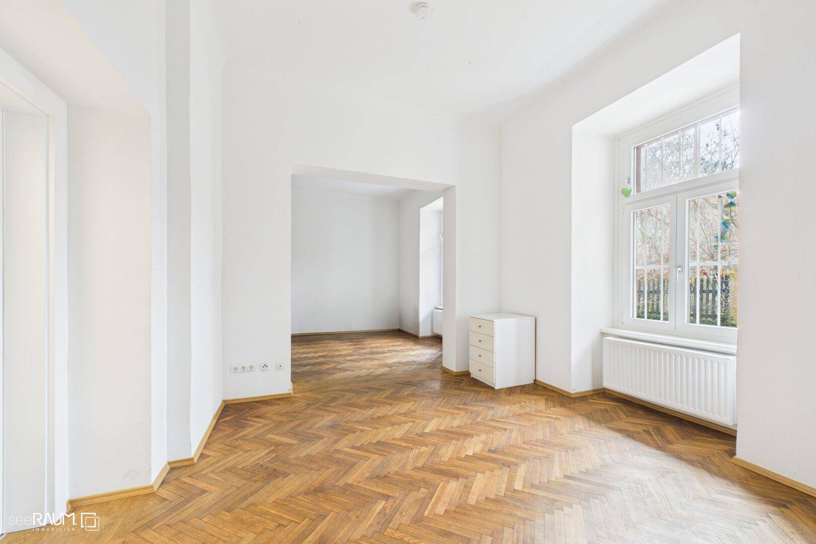 Leerer Raum mit Fischgrätparkett, hohen Decken und großem Fenster, bietet viel Gestaltungspotenzial.