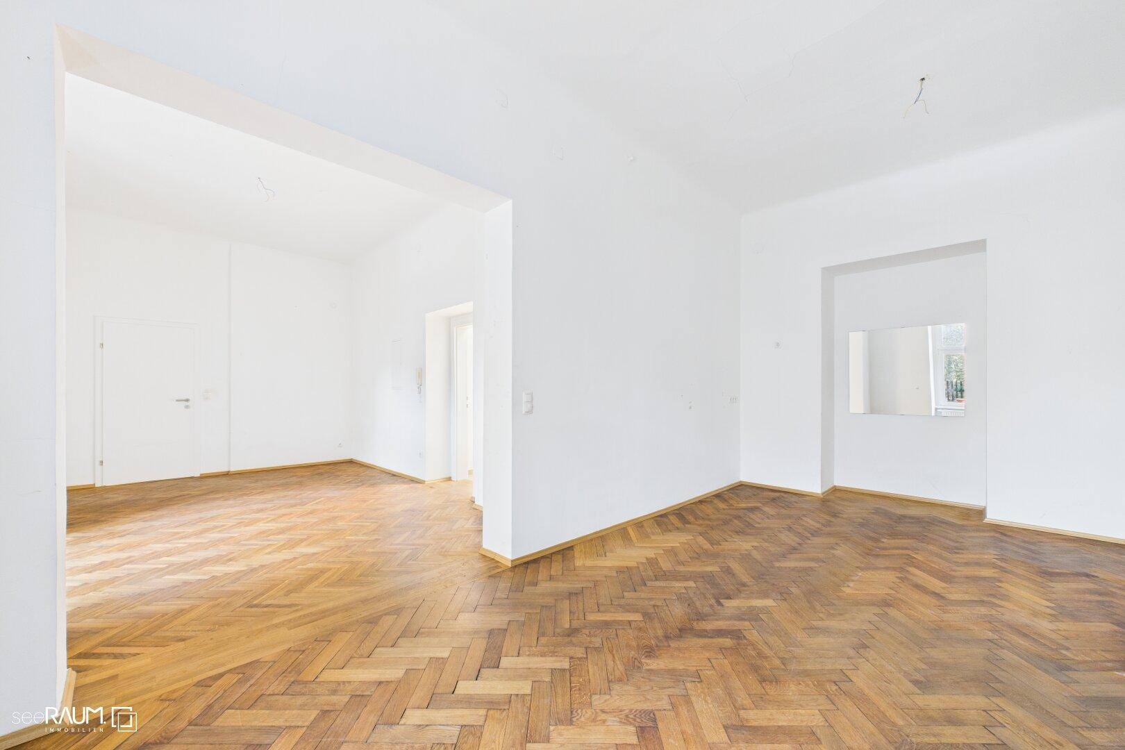 Geräumiger, leerer Raum mit Fischgrätparkett und hohen Decken, bereit zur individuellen Gestaltung.